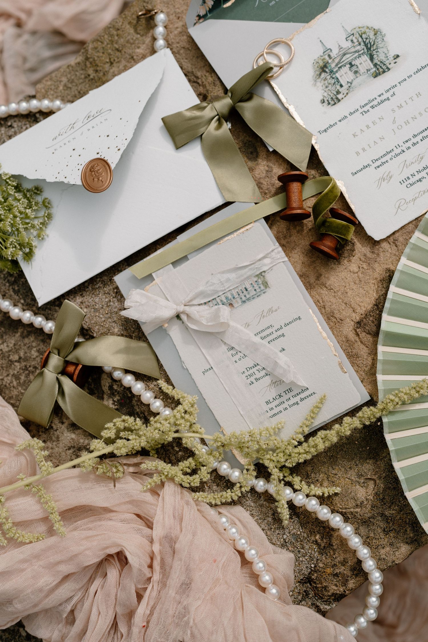Elegant wedding stationery flatlay with green ribbons, pearls, and wax seal envelope.