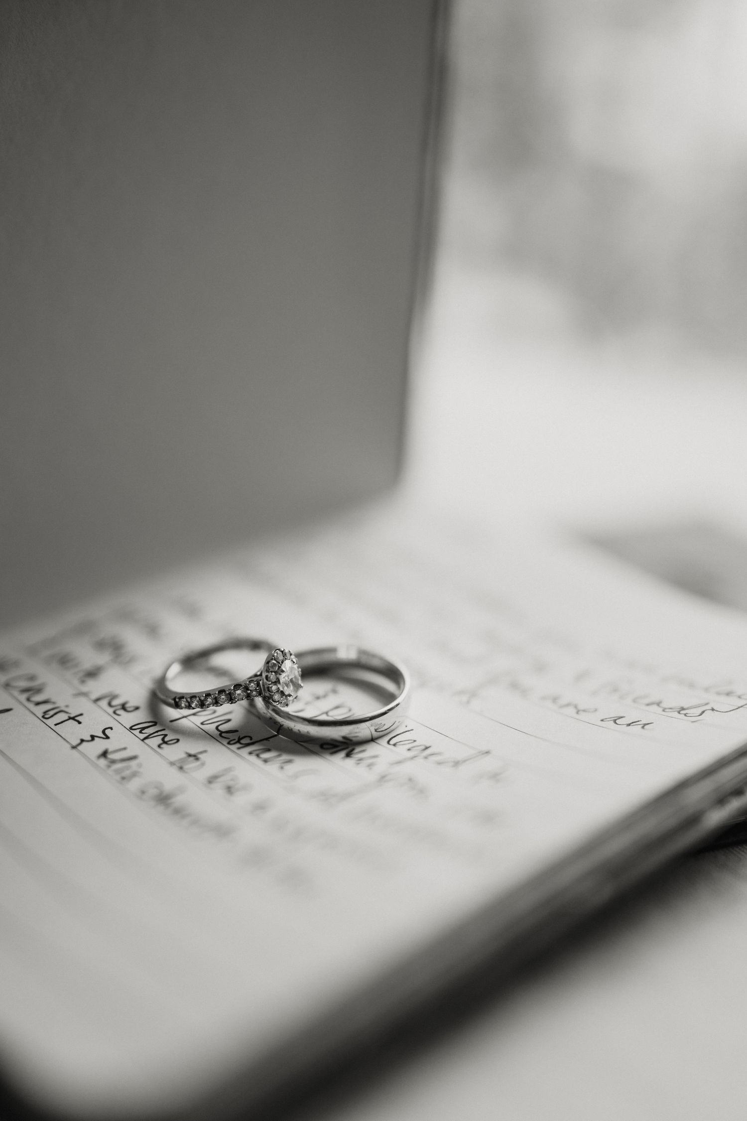 Black and white close-up of diamond engagement ring and wedding band on handwritten journal.