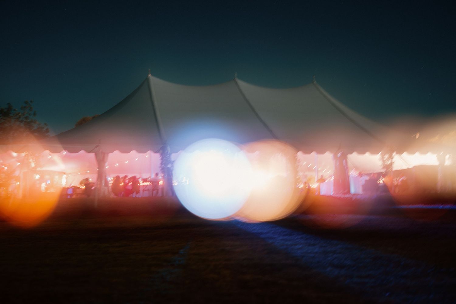 A glowing white wedding tent illuminated at night with colorful bokeh light effects outdoors.