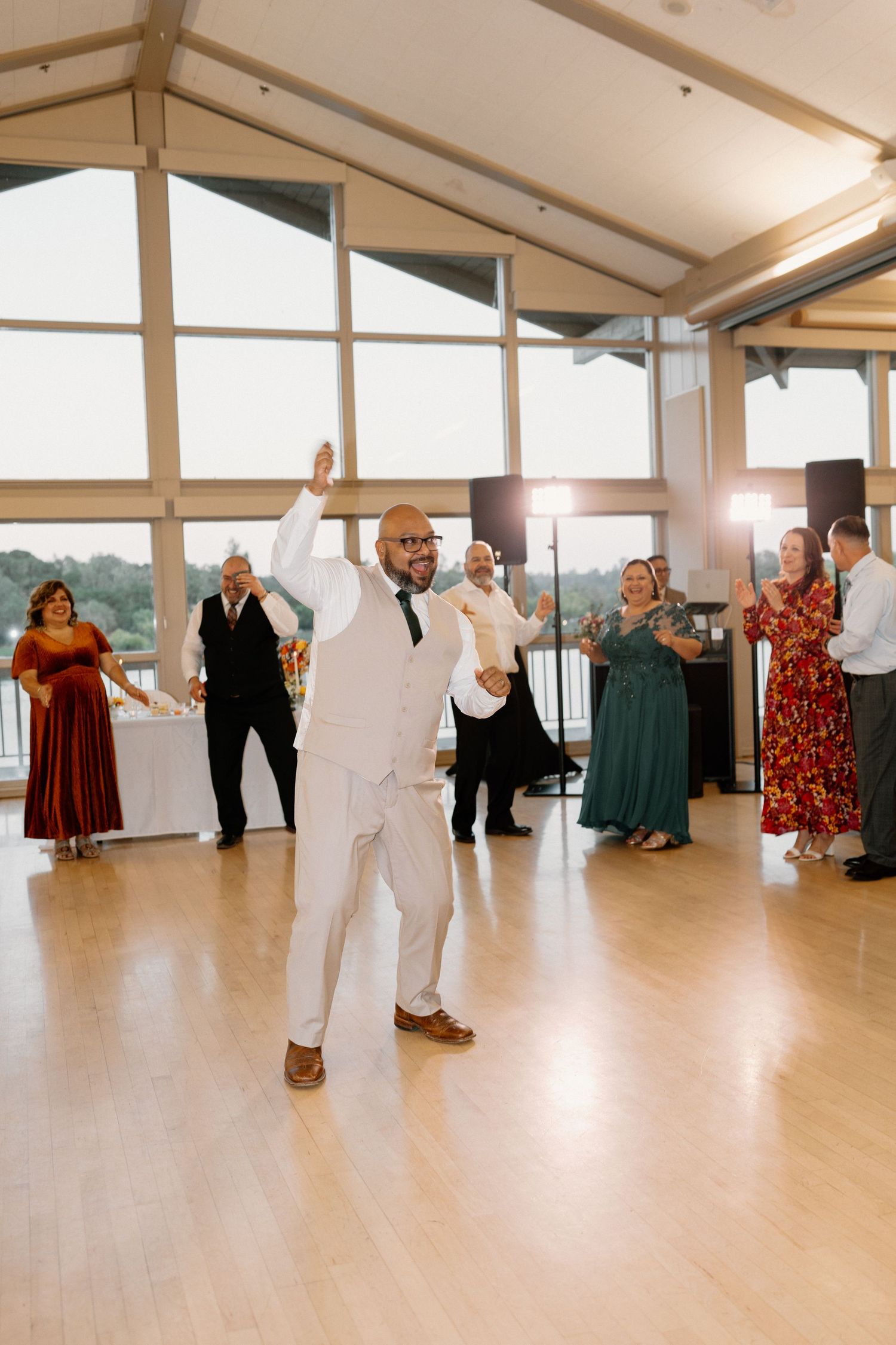 Groom in white suit celebrates on dance floor with raised arm at wedding reception.