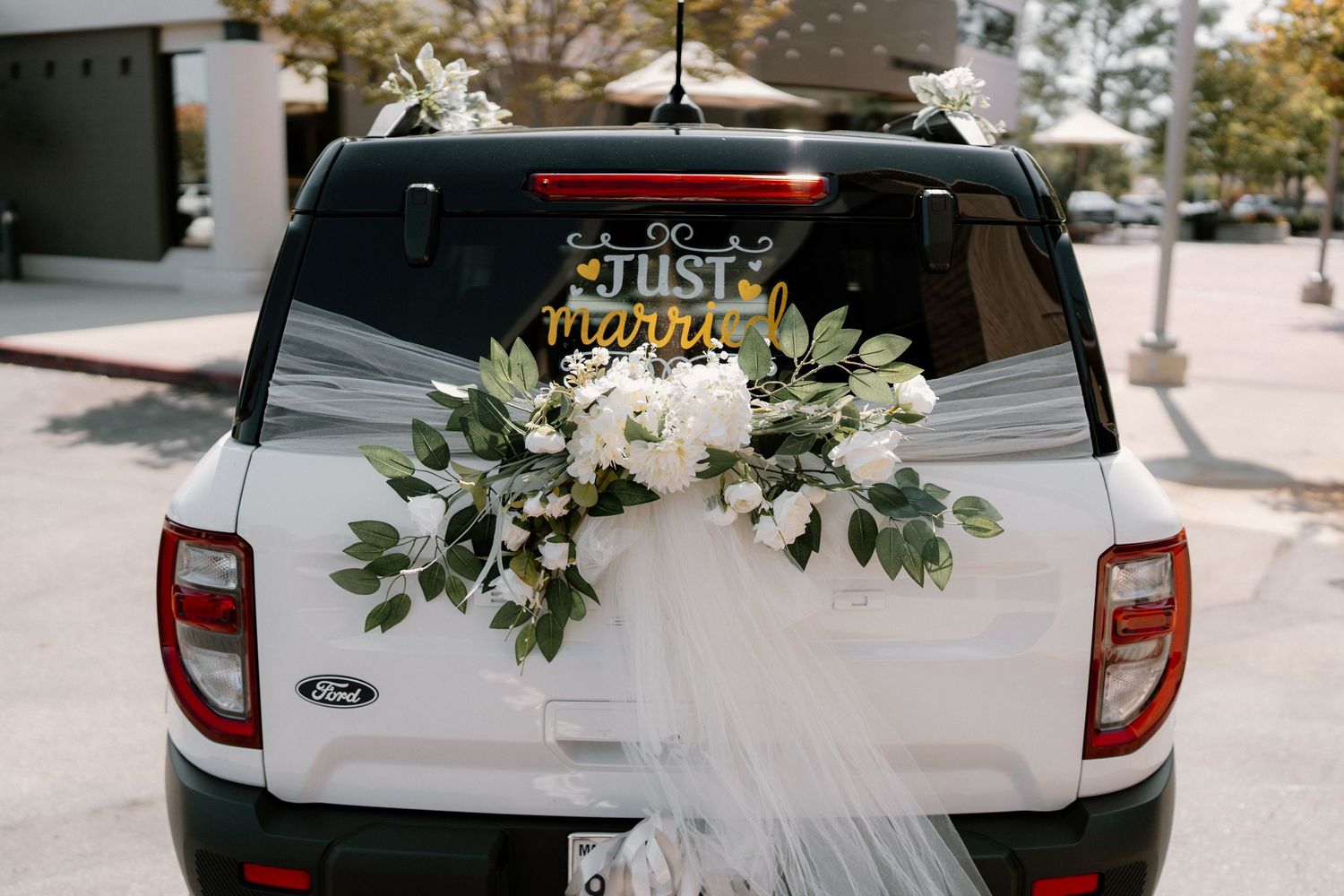 White Ford SUV decorated with Just Married sign, white floral arrangement, and tulle for a wedding getaway car.