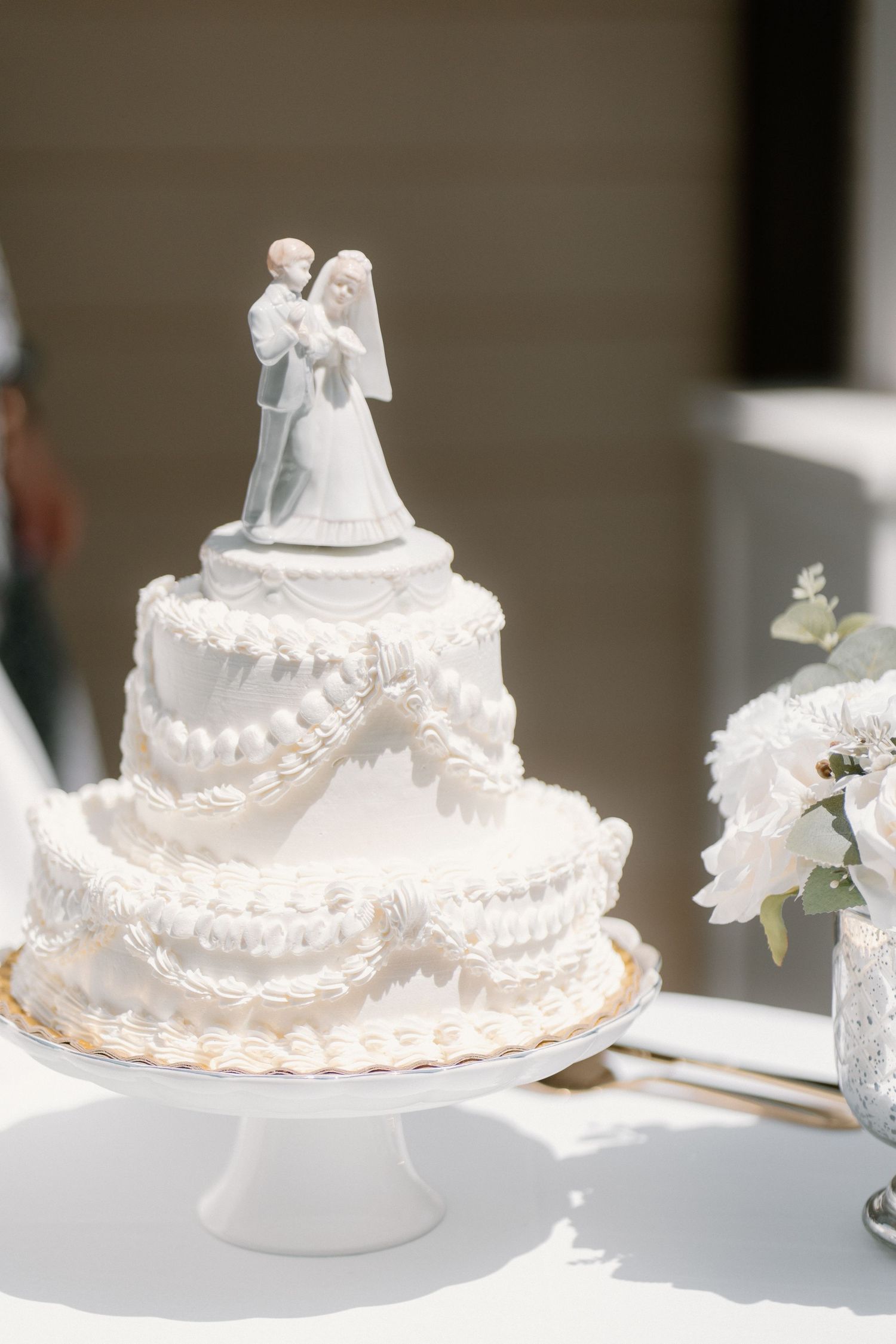 Elegant three-tier white wedding cake topped with a classic bride and groom figurine on a cake stand.