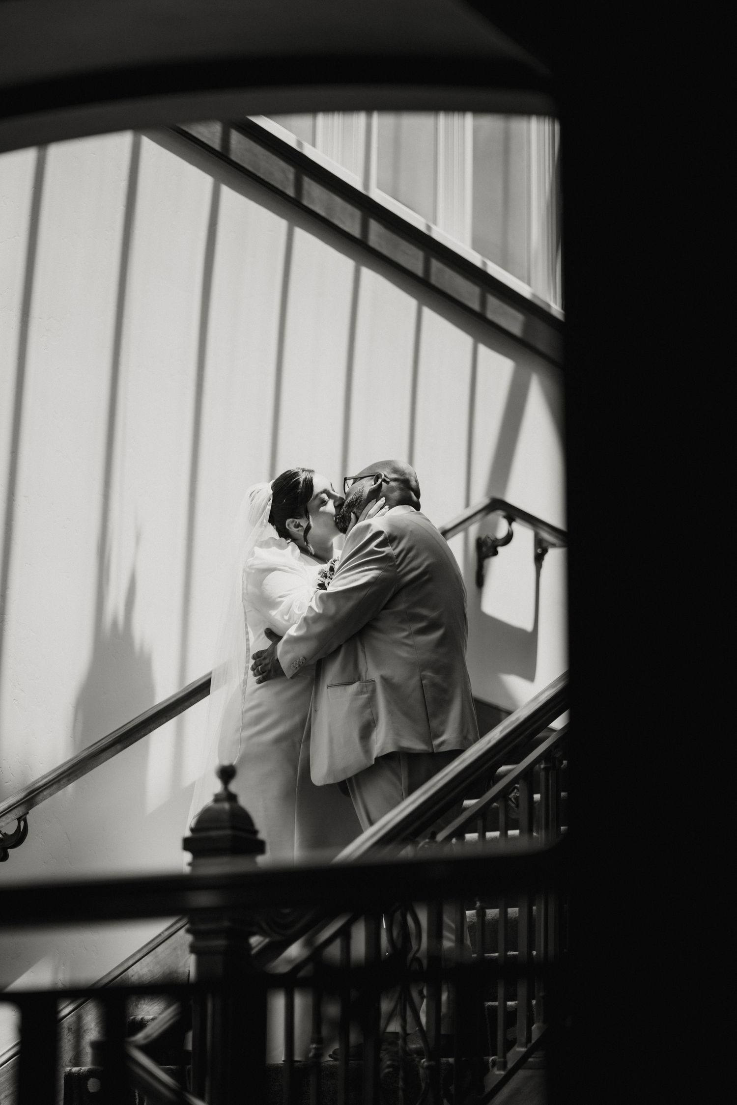 Black and white photo of bride and groom sharing a kiss on a staircase at their wedding.