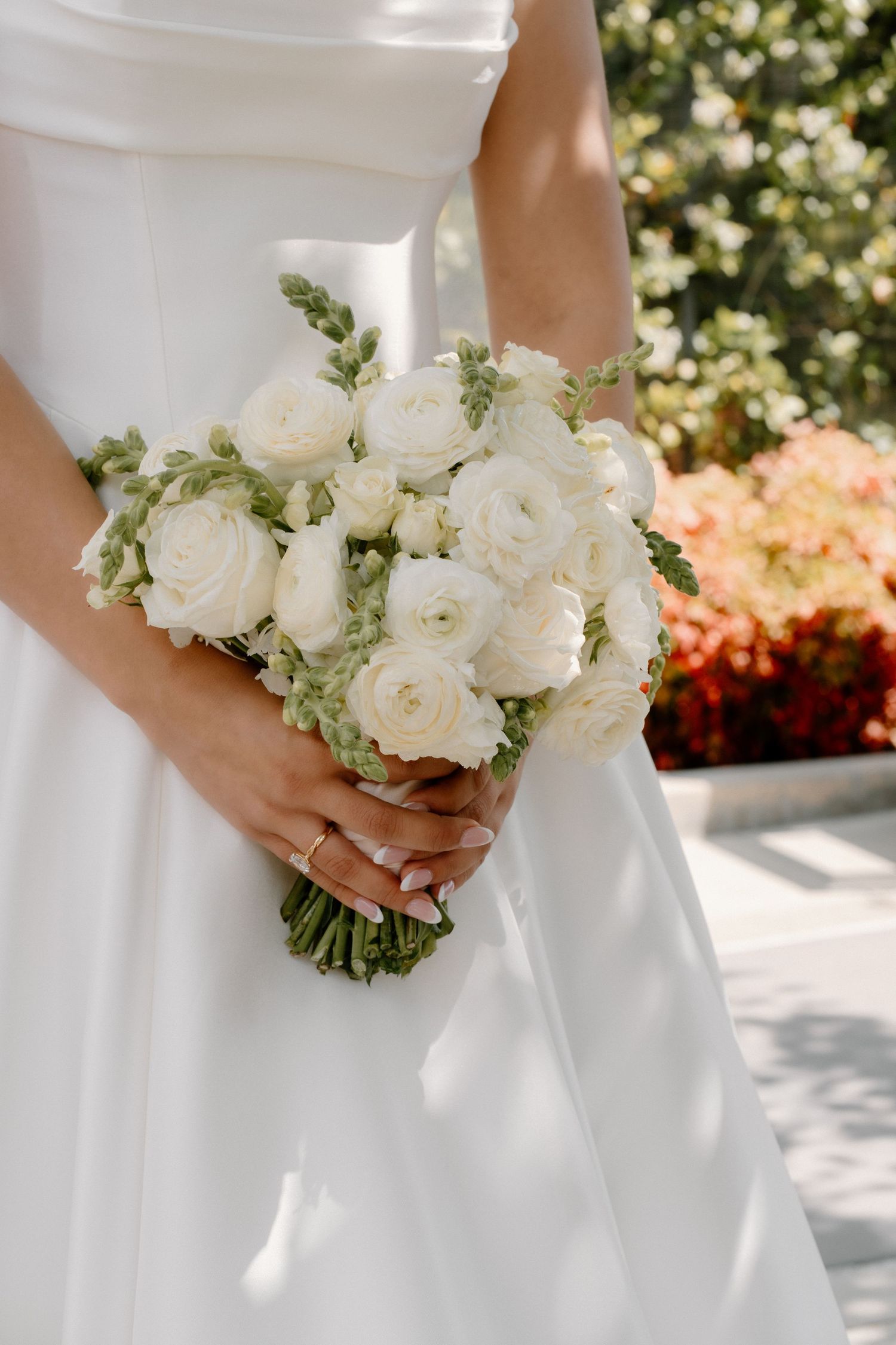 Bride holding elegant white ranunculus and greenery wedding bouquet against her white satin gown.