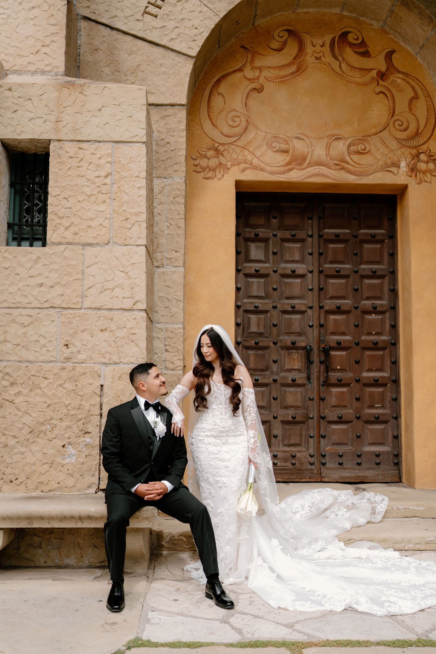 Bride and groom posing before ornate wooden door of historic stone building after ceremony.