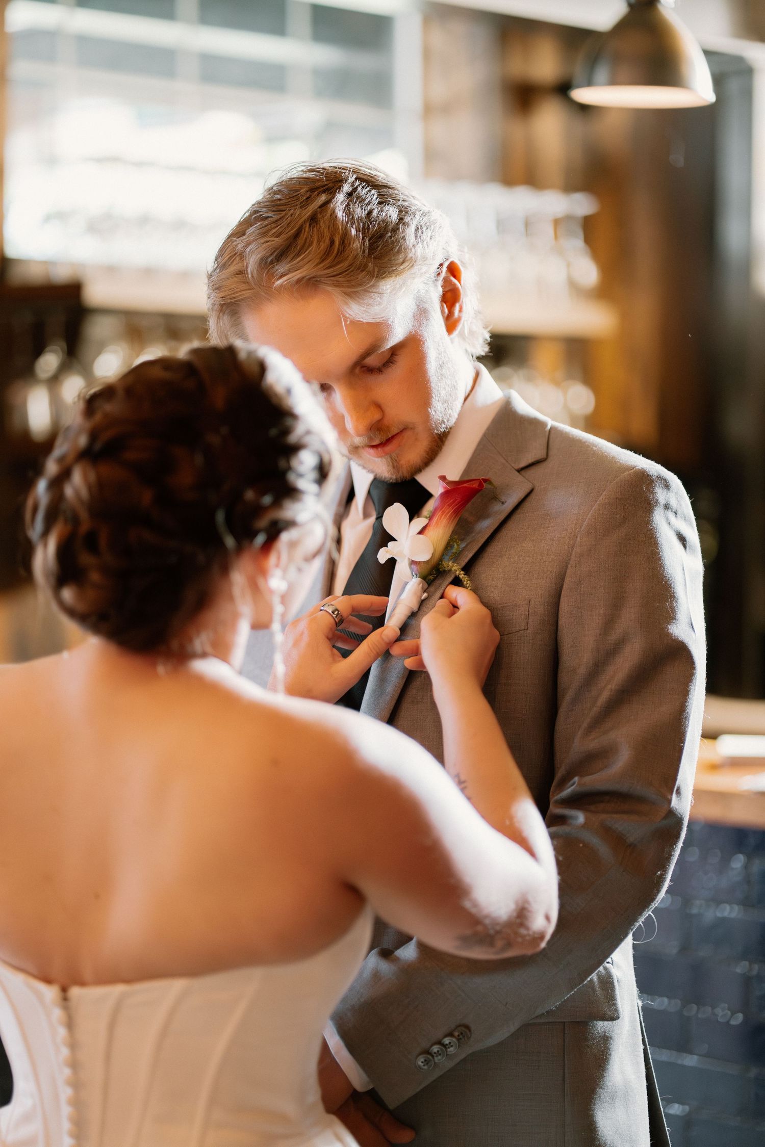 Bride pinning a red rose boutonniere on groom in gray suit before wedding ceremony.