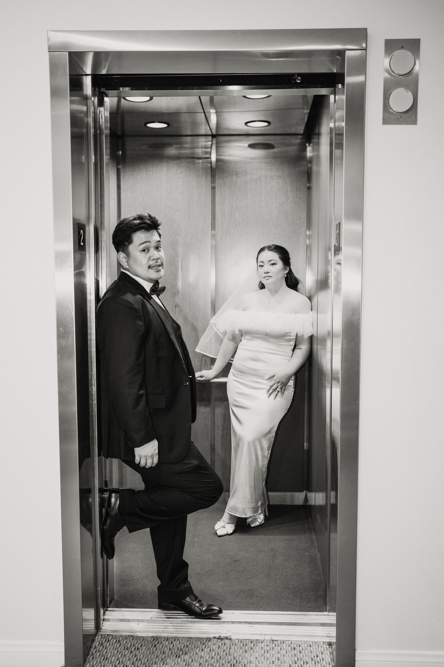 Bride and groom pose playfully inside an elevator in a black and white wedding photo.