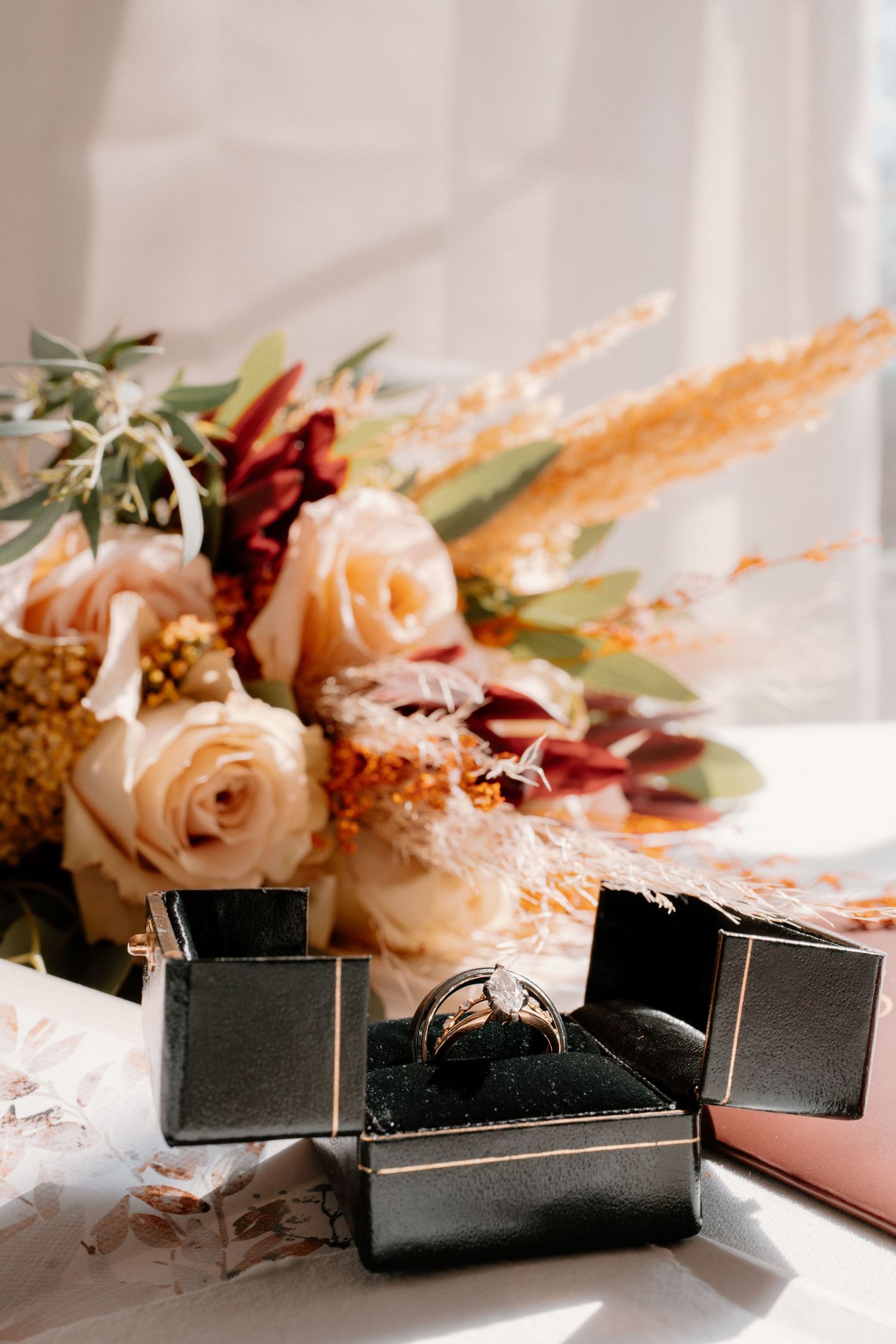 Diamond engagement ring in open black velvet box beside a bouquet of peach roses and dried autumn florals.