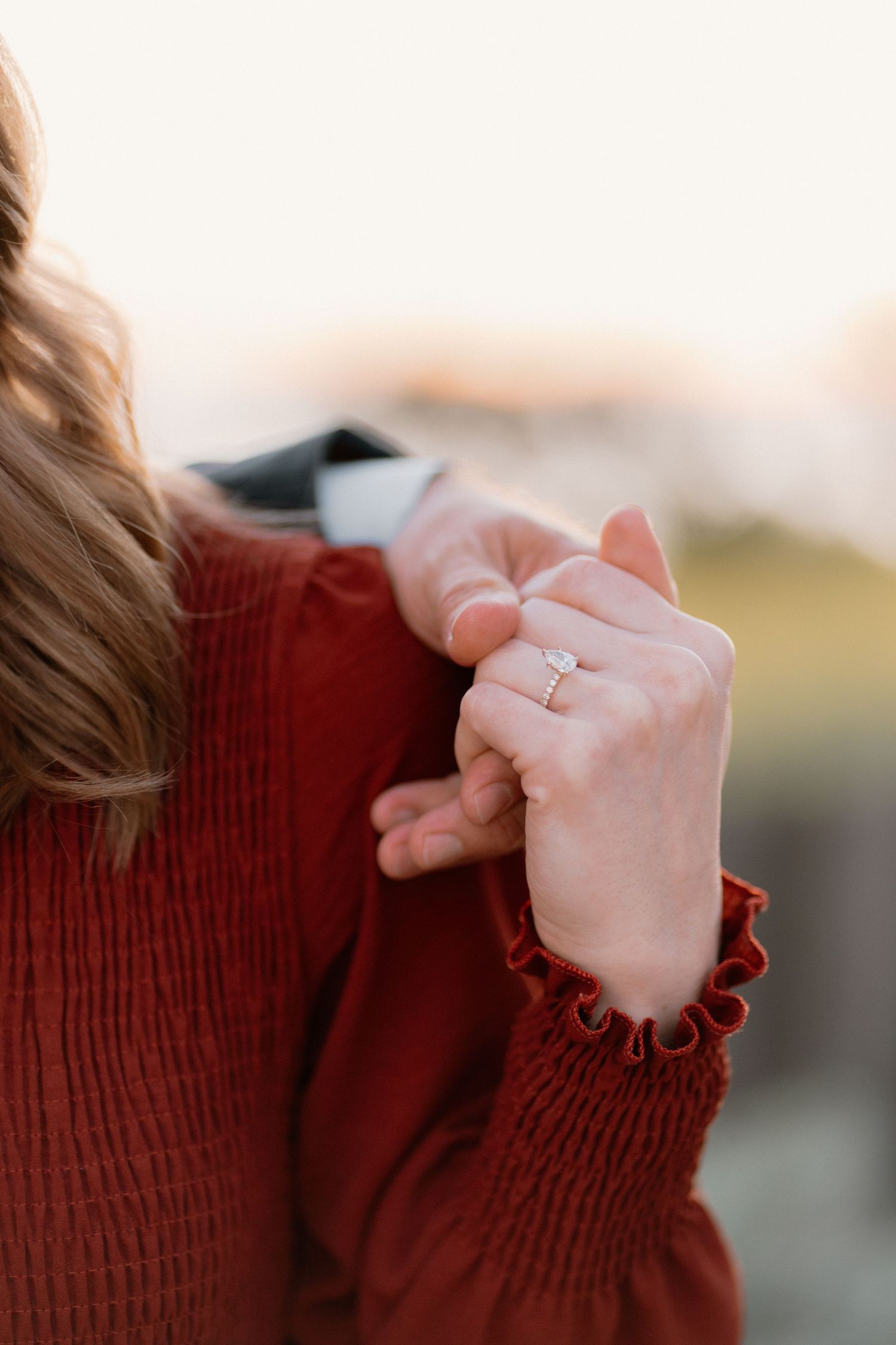 Close-up of a diamond engagement ring on a woman's hand in red dress.