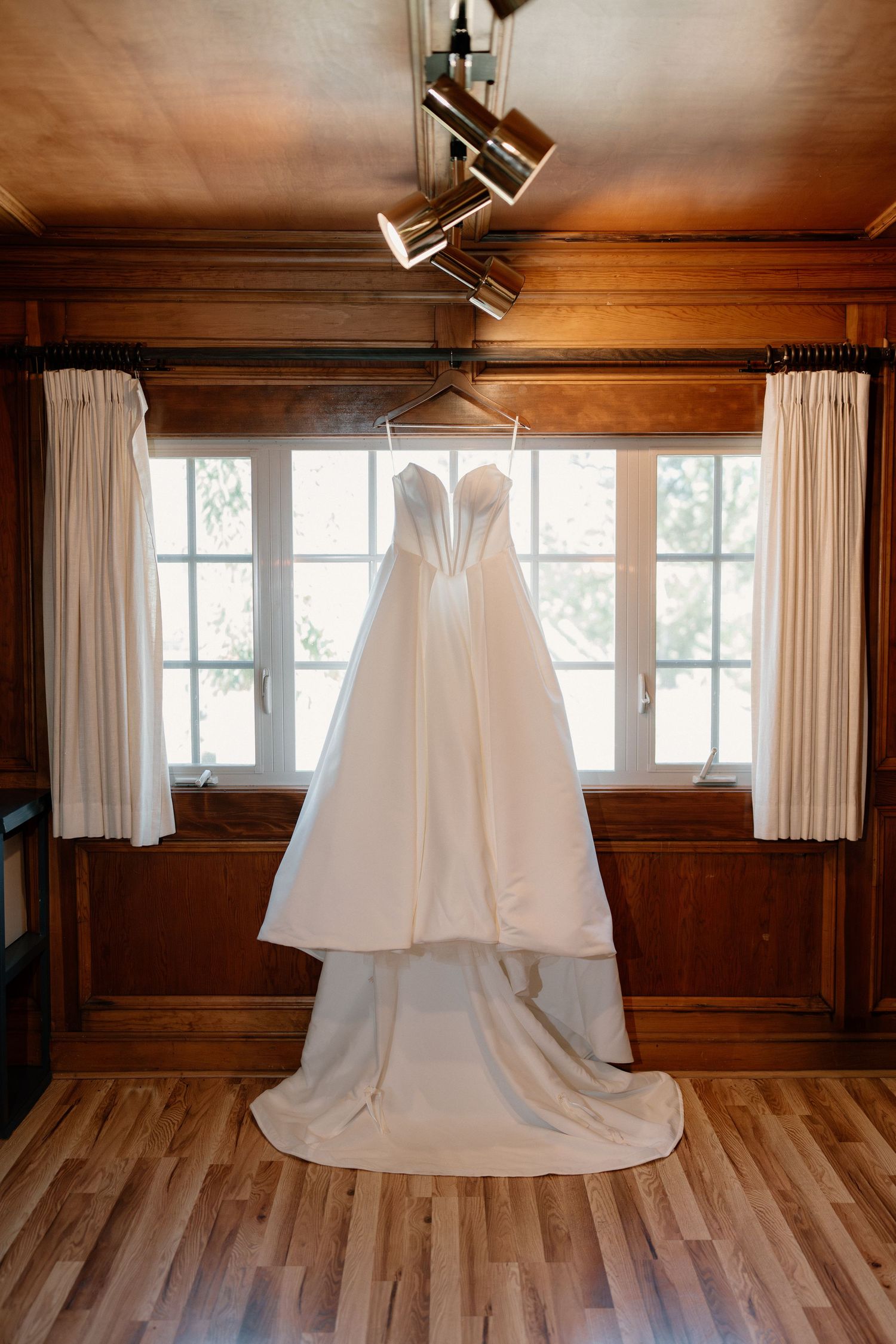 White strapless ball gown wedding dress hanging in rustic wood-paneled bridal suite.