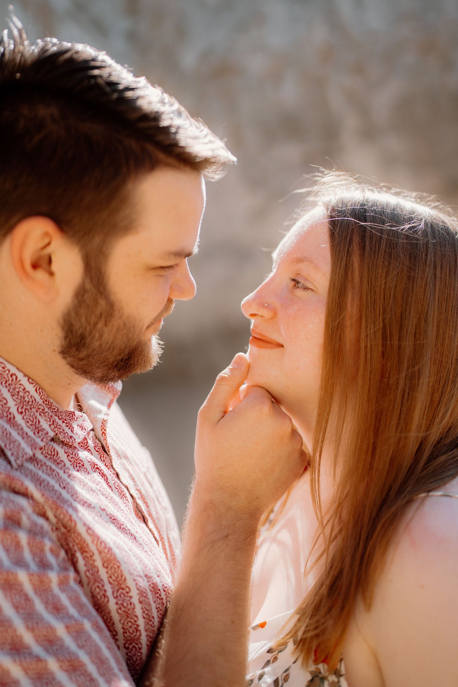 Bearded man gently cupping womans chin as they gaze into each others eyes in sunlight.