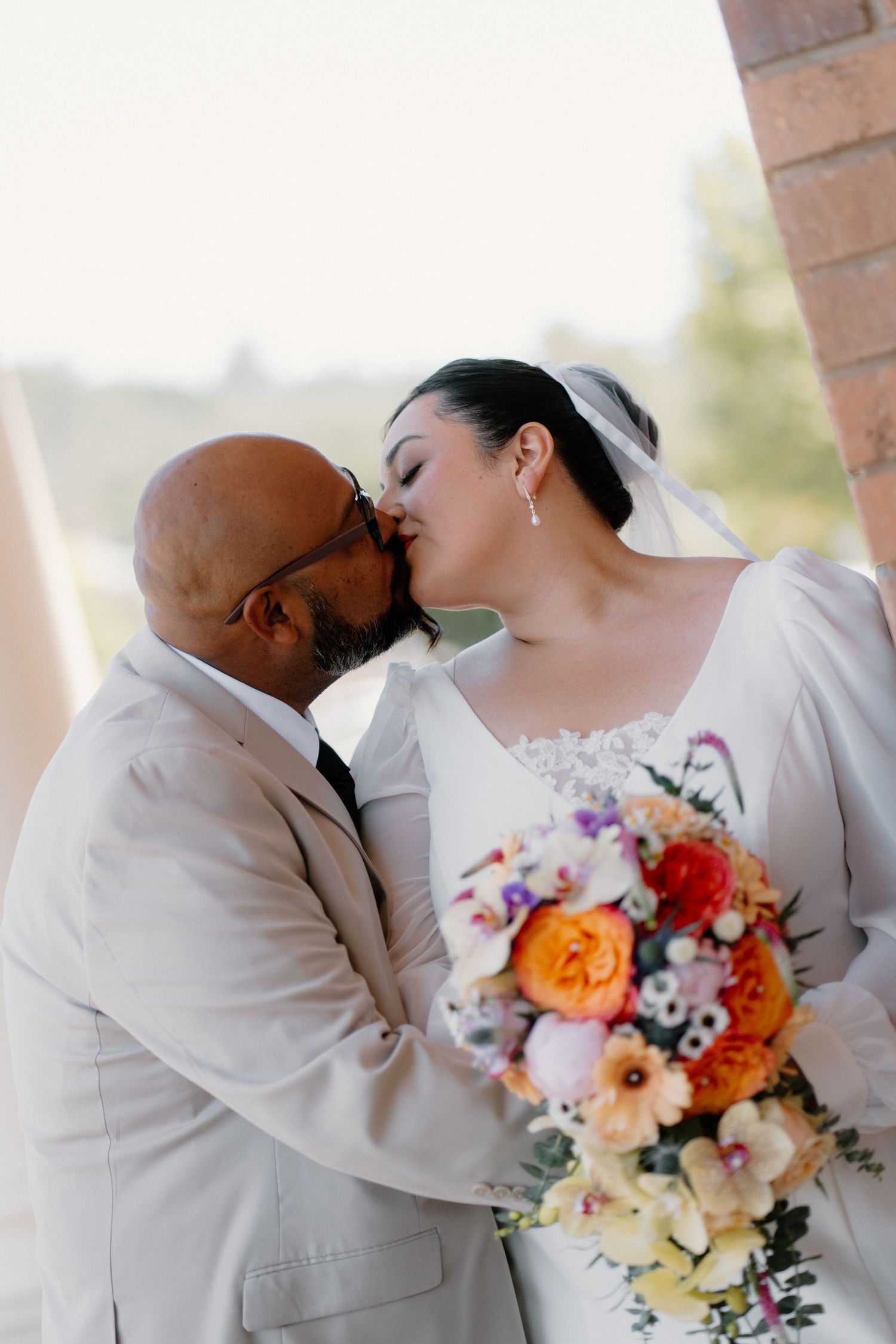 Bride and groom share a kiss holding colorful wedding bouquet at elegant venue.