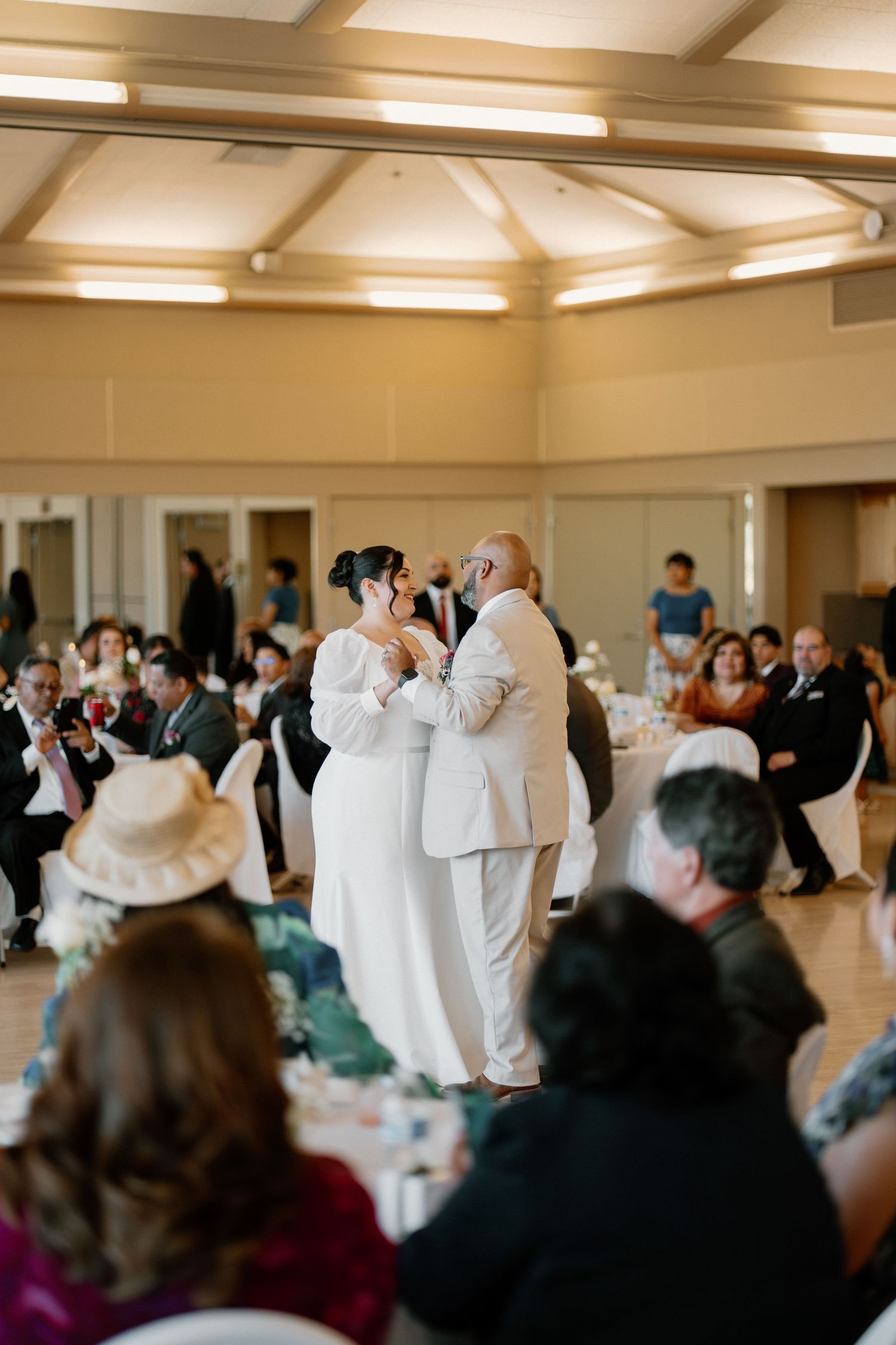 Bride and groom share their first dance at wedding reception while guests watch in elegant banquet hall.