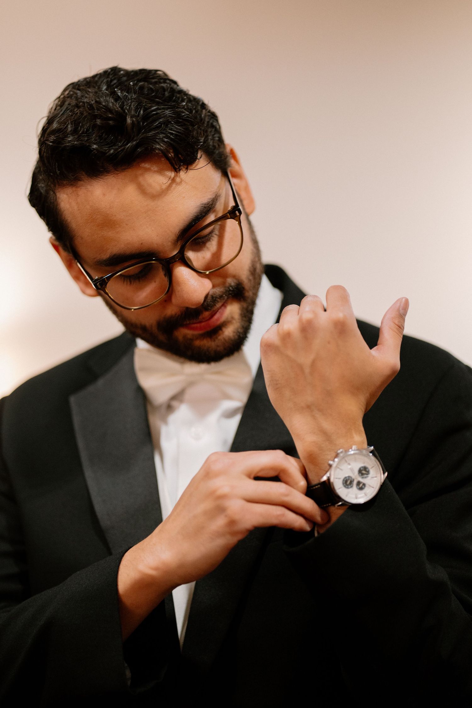 Dapper groom in tuxedo adjusting watch while getting ready for wedding ceremony.