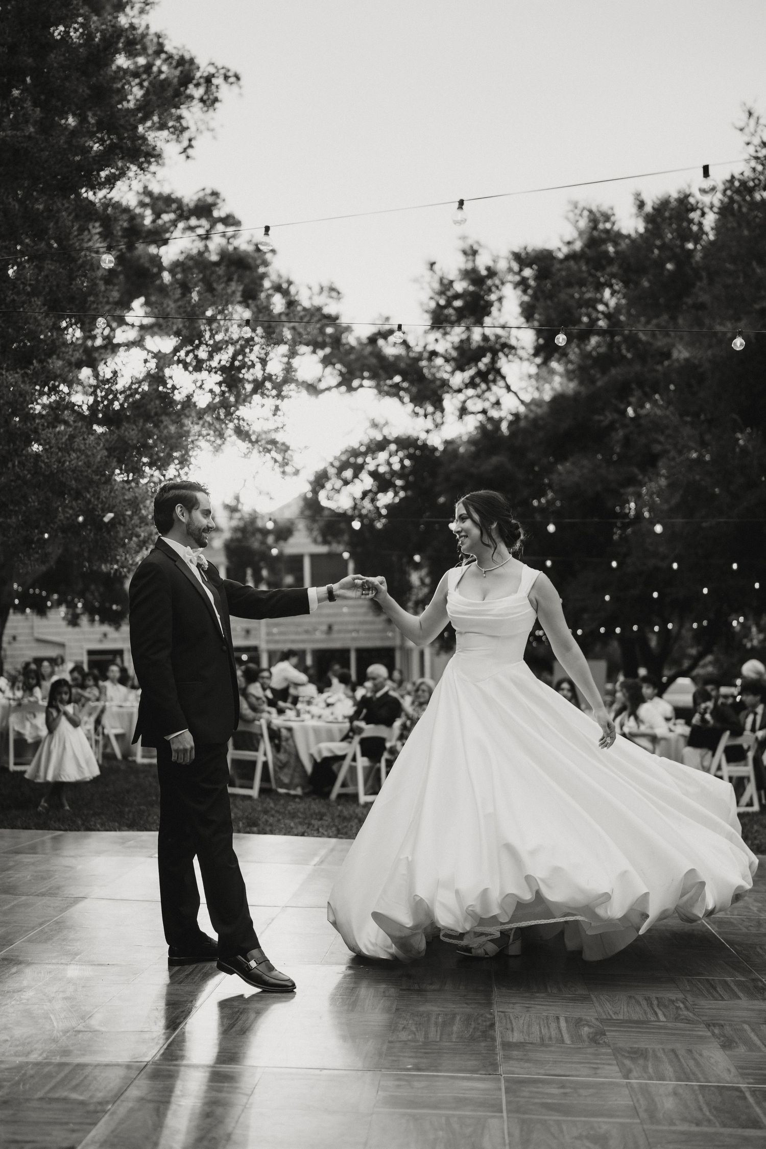 Black and white photo of bride and groom sharing first dance at outdoor wedding reception.