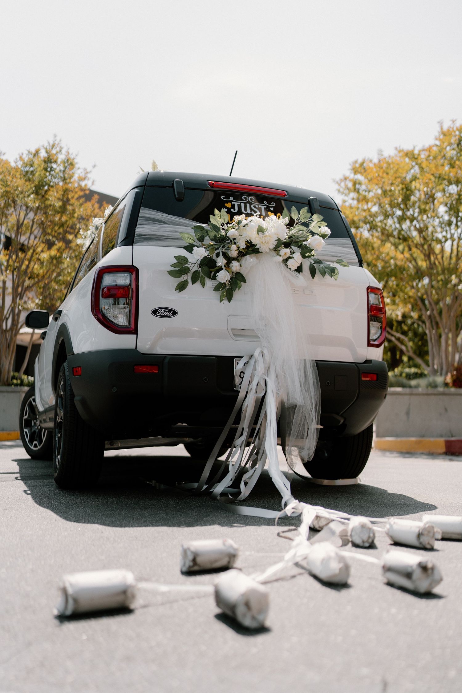 White Ford truck decorated with floral arrangement, white ribbons, and tin cans as wedding getaway car.