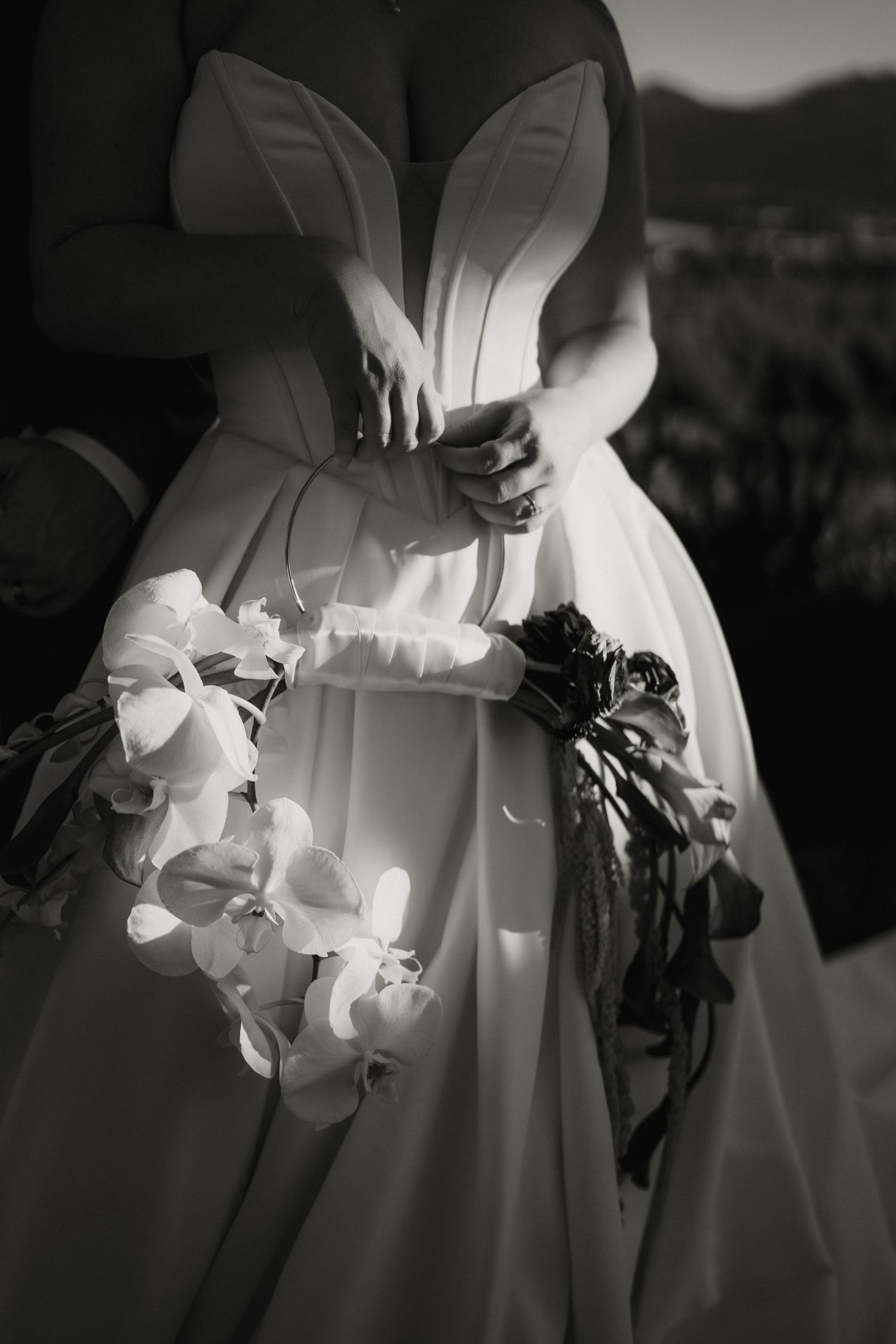 Close-up black and white photo of bride holding white orchid bouquet in elegant structured wedding gown.