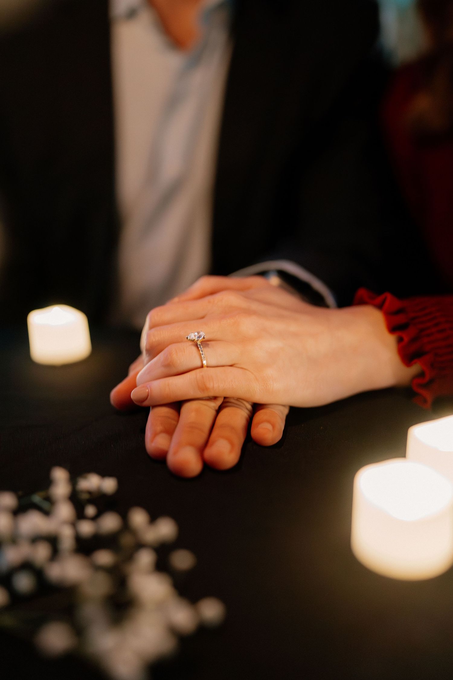 Close-up of engaged couple's hands with a diamond ring surrounded by glowing candles.
