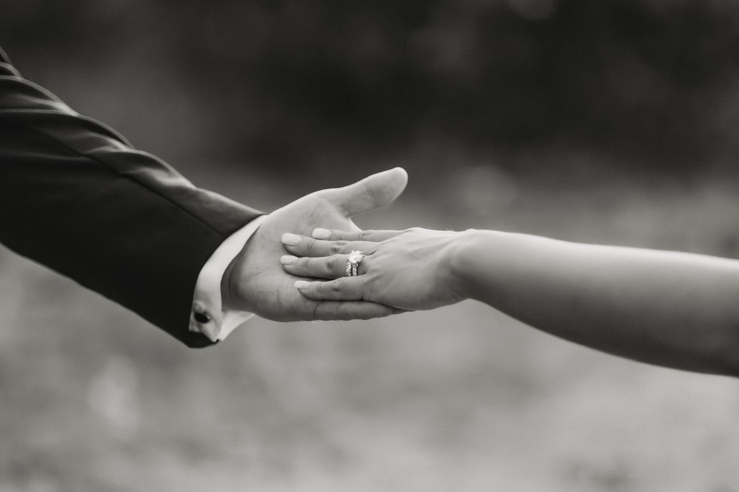 Black and white close-up of bride and groom holding hands showing wedding rings during their ceremony.
