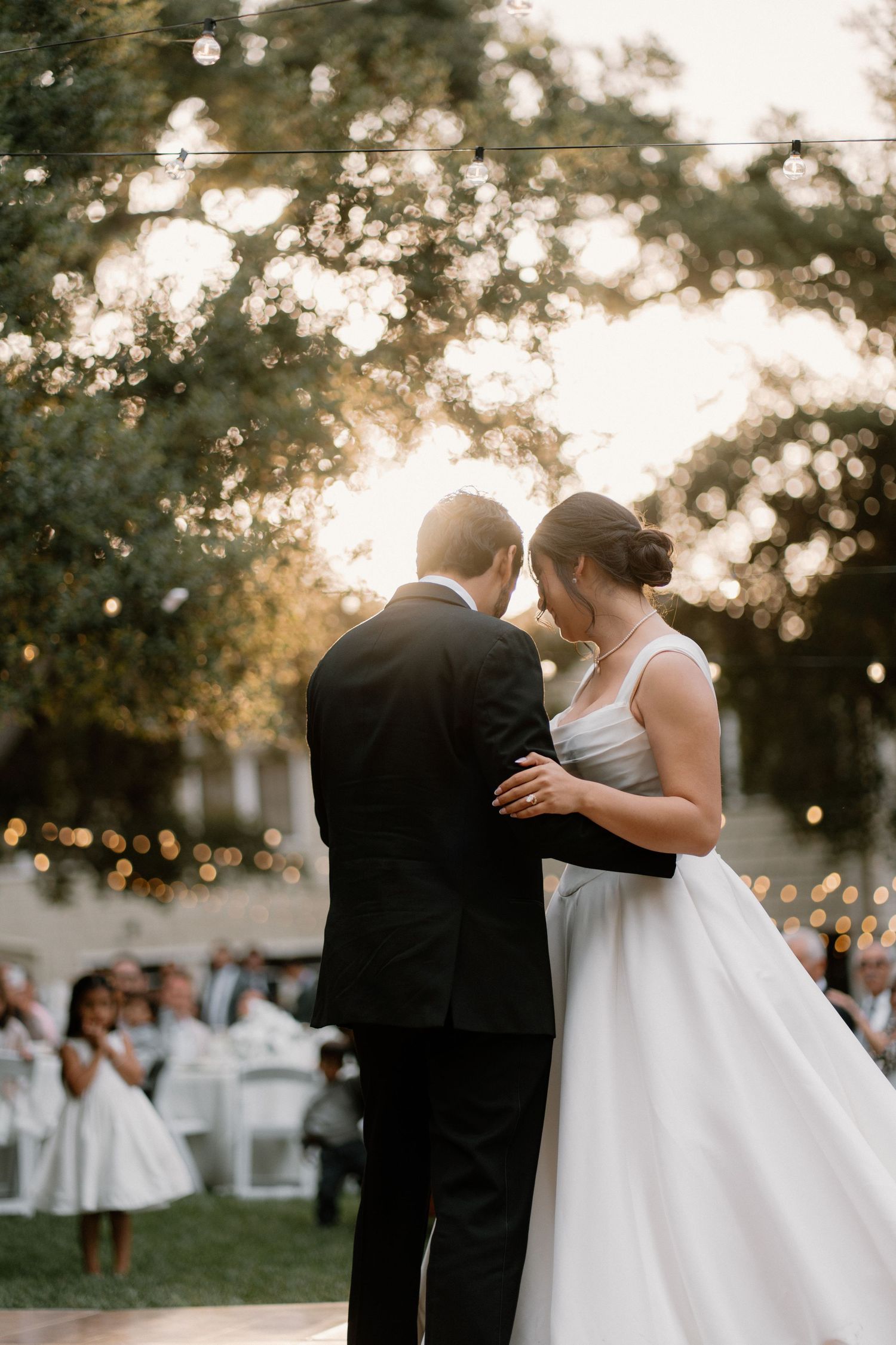 Bride and groom share intimate first dance outdoors under string lights at golden hour wedding.
