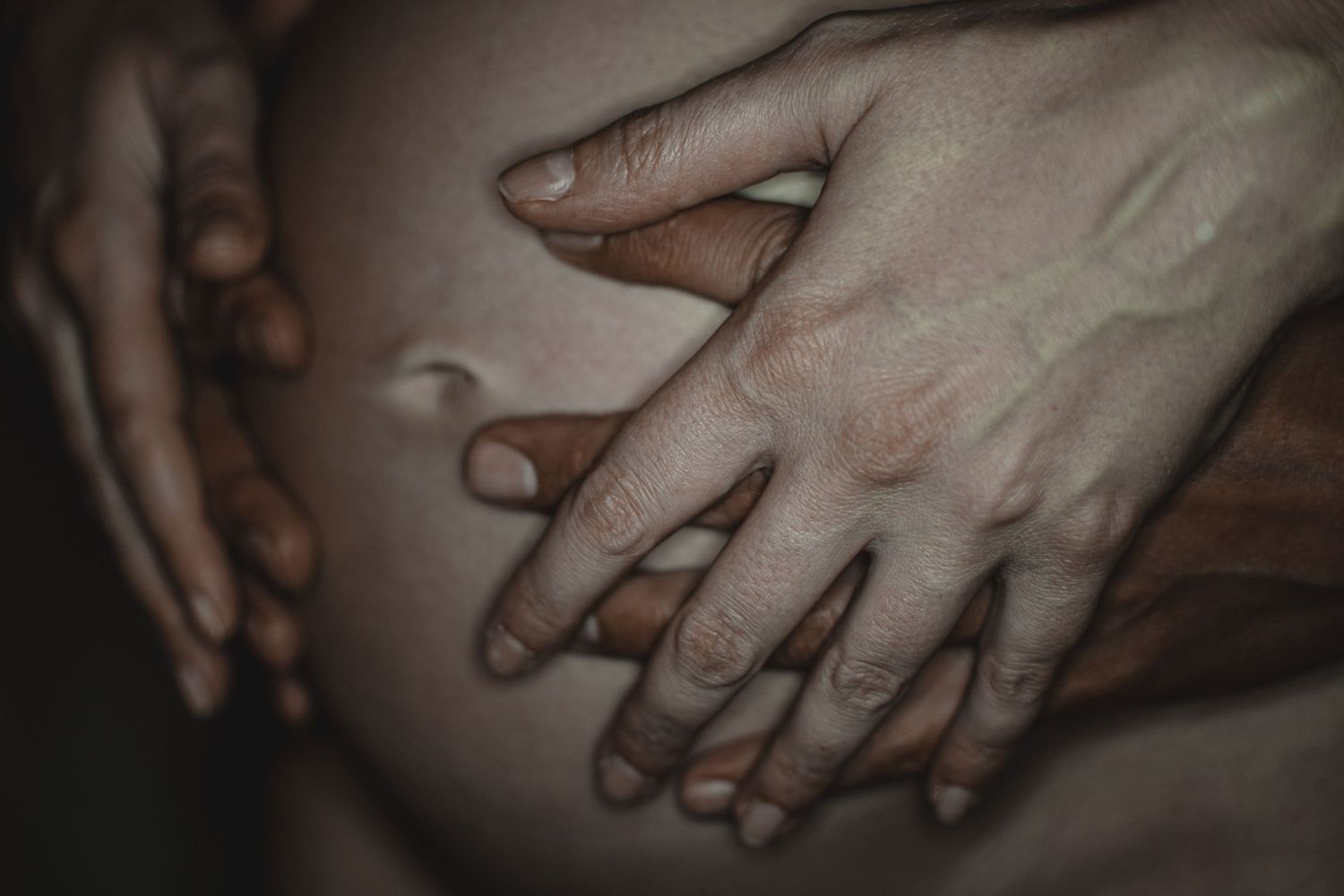 Mehrere Hände liegen liebevoll auf einem Babybauch