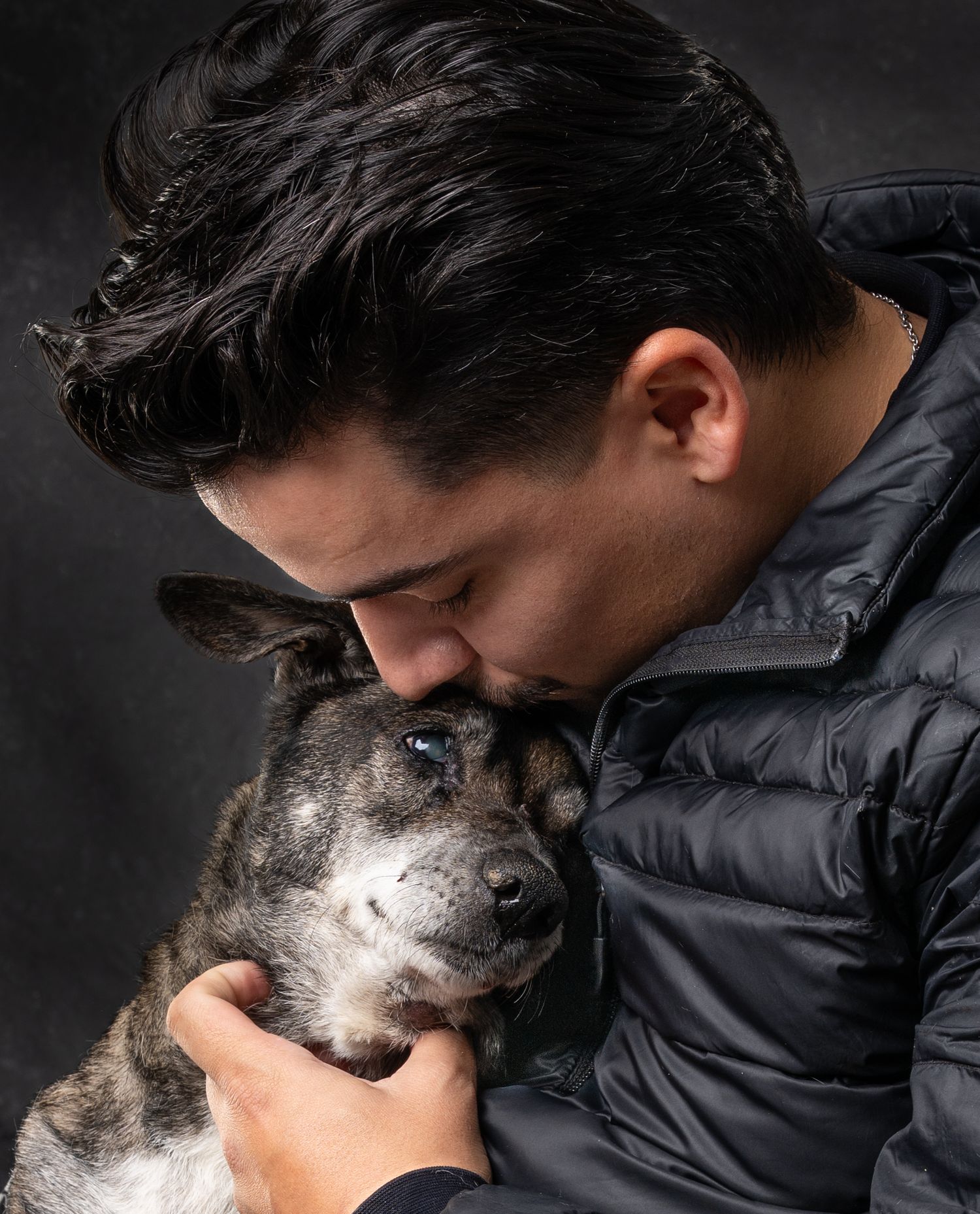A man kissing his senior brindle dog affectionately.
