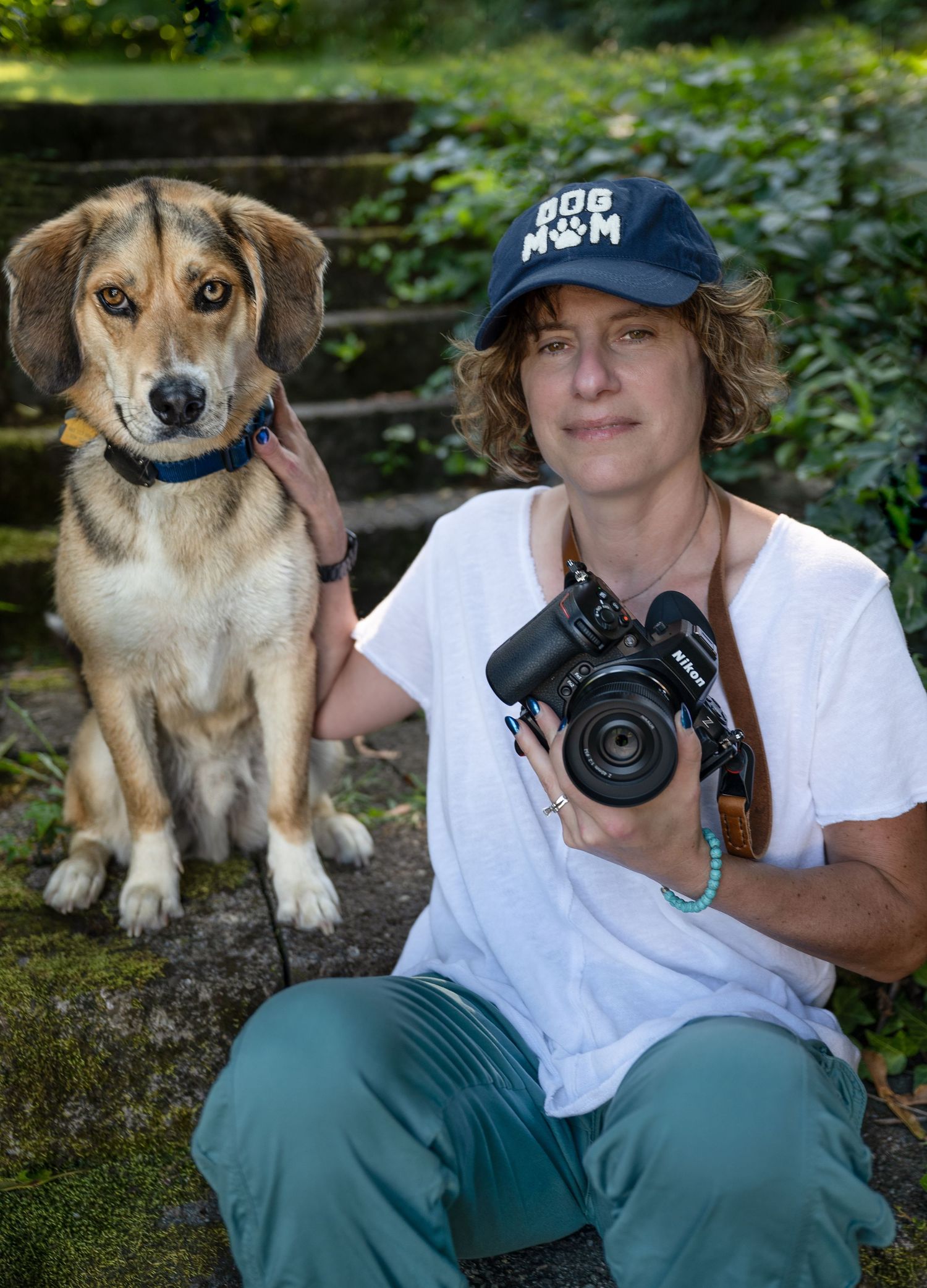 Female pet photographer posing with a beagle mix dog while holding a Nikon camera outdoors.