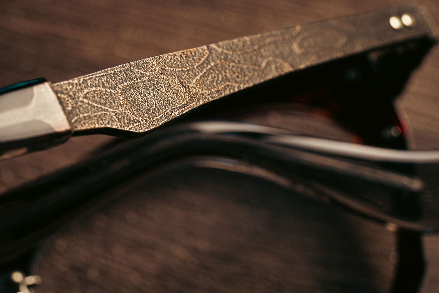 Close-up of decorative engraved gold sunglasses arm with floral pattern resting on dark wooden surface.