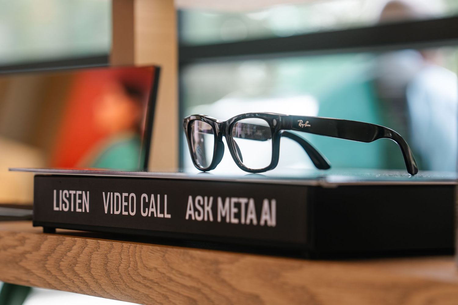 Ray-Ban Meta AI smart glasses resting on a black display box labeled Listen, Video Call, Ask Meta AI.