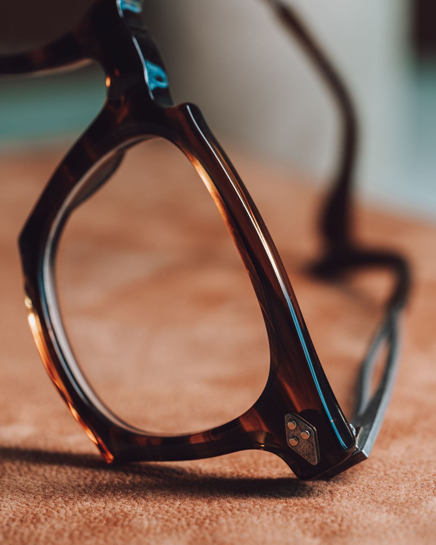 Close-up of tortoiseshell eyeglasses frame resting on a brown surface, showcasing rich amber and dark brown acetate details.