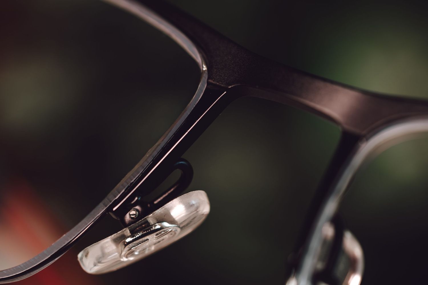 Close-up macro shot of black eyeglass frames showing nose pad and hinge detail on blurred green background.