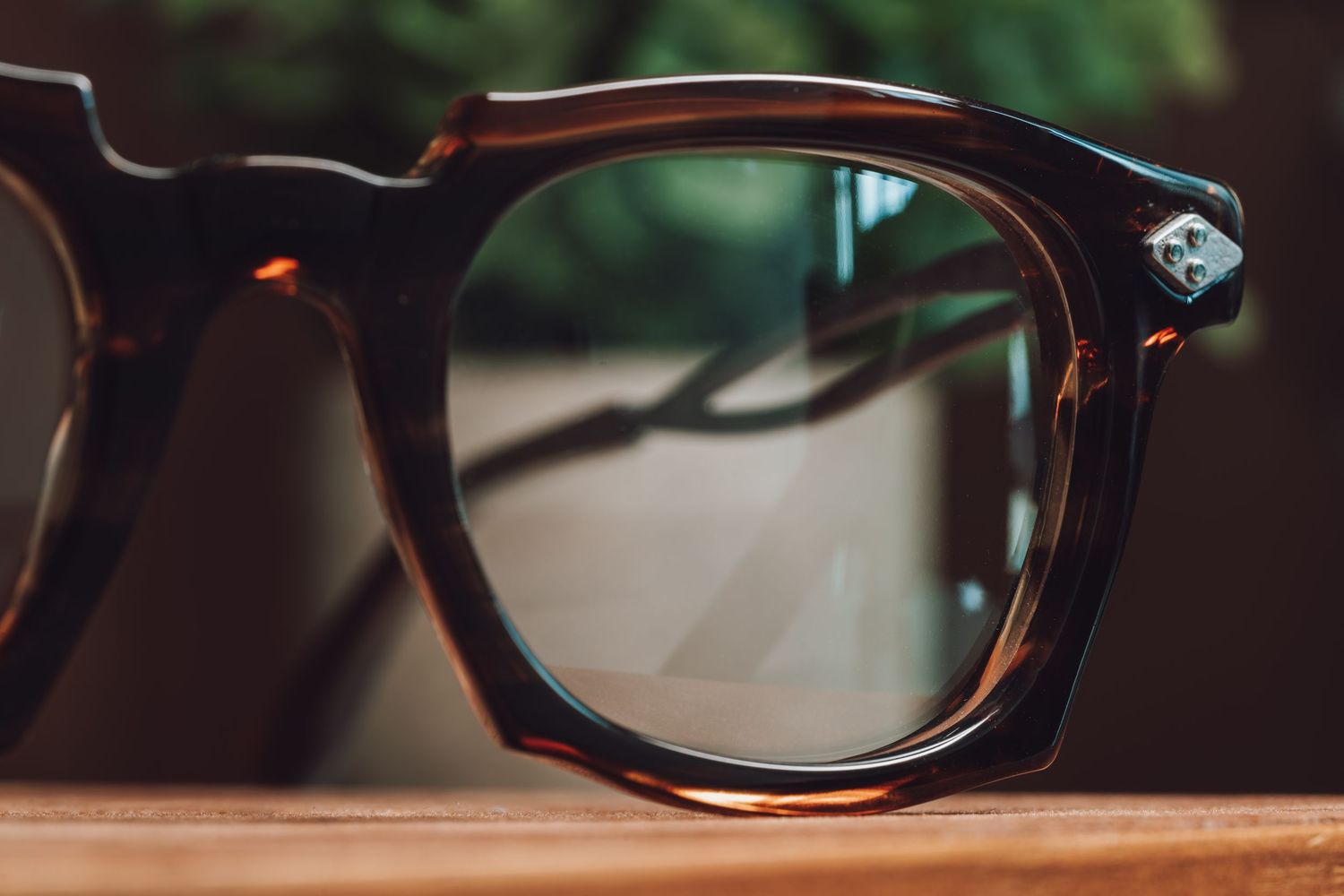 Close-up of vintage tortoiseshell wayfarer eyeglasses resting on a wooden surface with green bokeh background.
