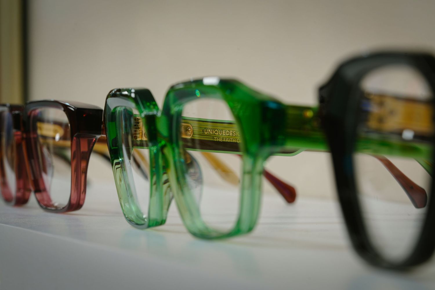 Colorful vintage eyeglass frames displayed in a row, featuring green, red, and dark acetate styles on a white surface.