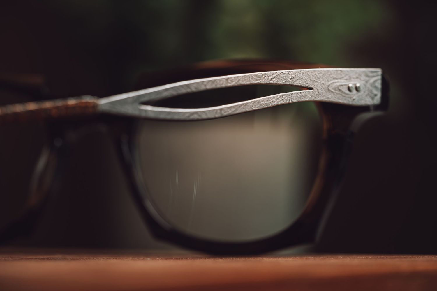 Close-up of stylish sunglasses with ornate silver patterned frames and reflective lenses resting on a wooden surface.