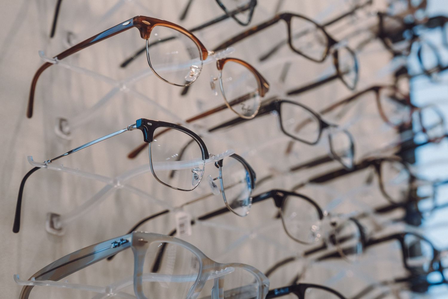 Multiple eyeglasses frames displayed on a wall-mounted rack in an optical store, showcasing various styles and colors.