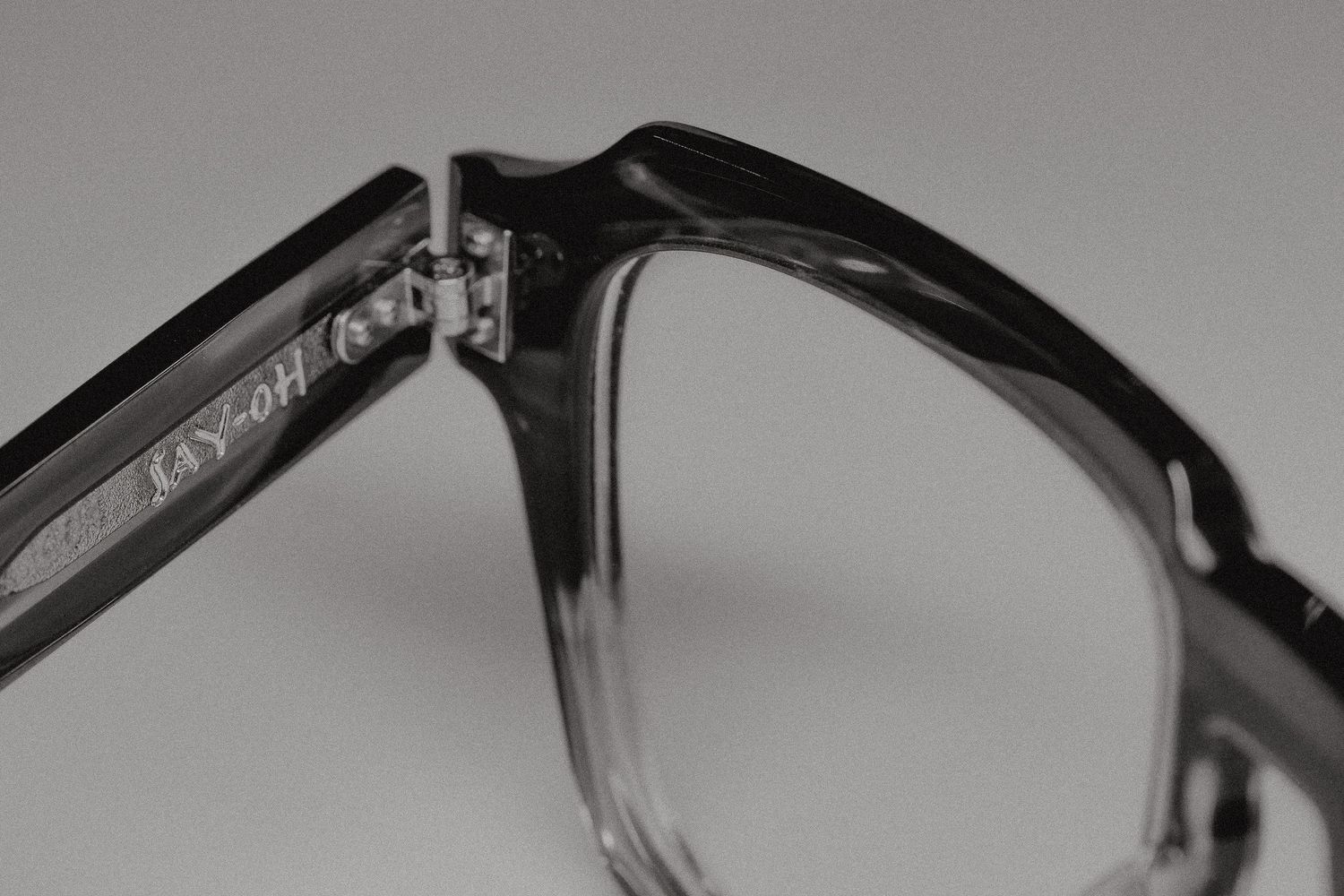 Close-up black and white photo of stylish acetate eyeglass frames showing bridge detail and brand engraving.