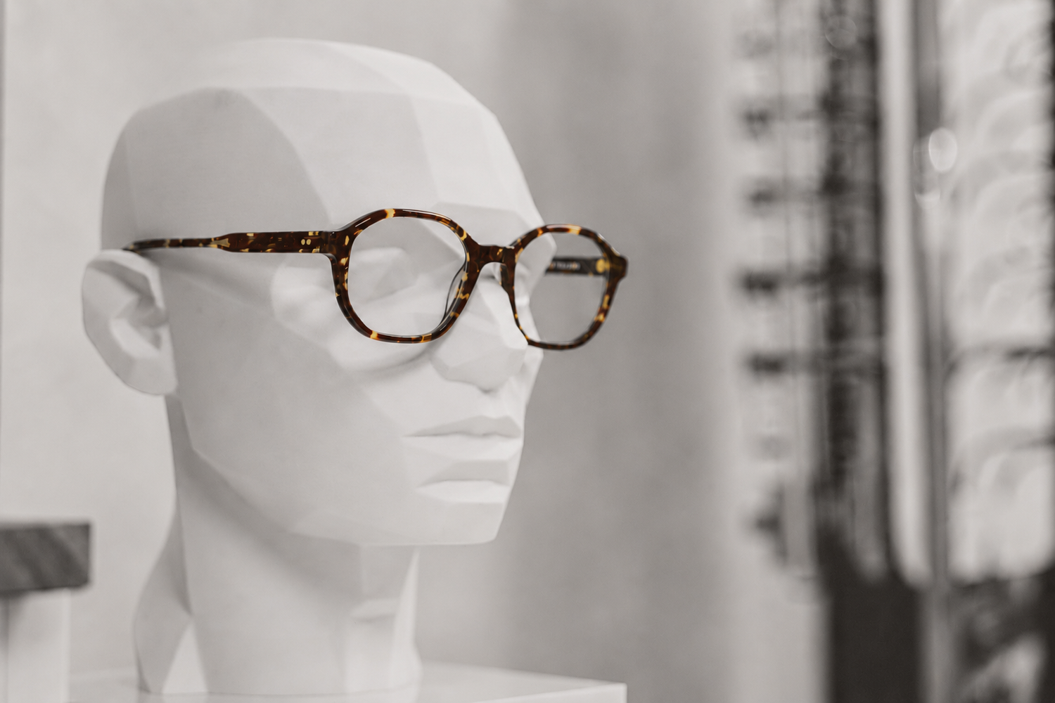 White mannequin head displaying stylish tortoiseshell glasses in an optical store window display.