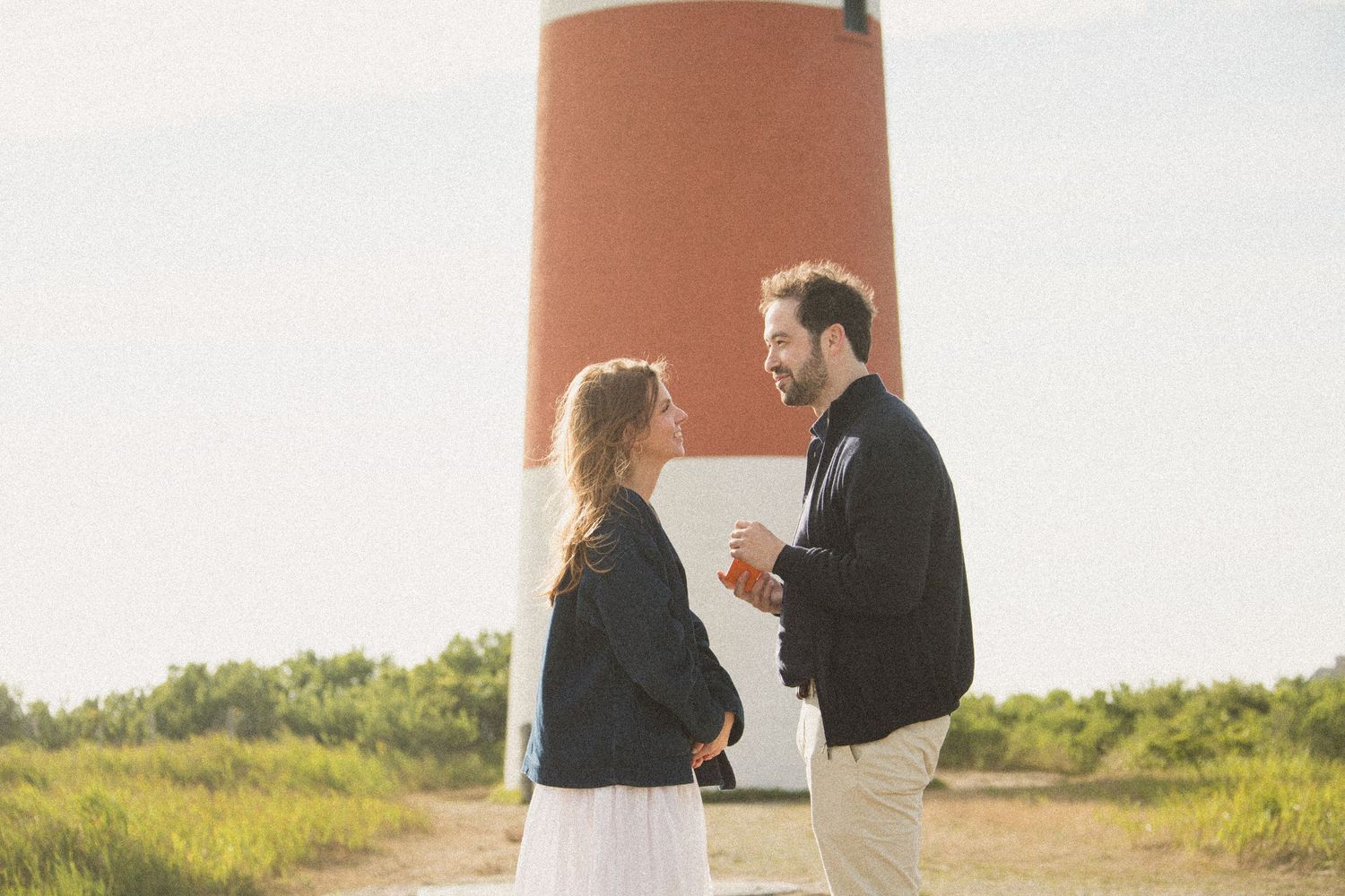 Red and white lighthouse provides backdrop for romantic coastal moment.