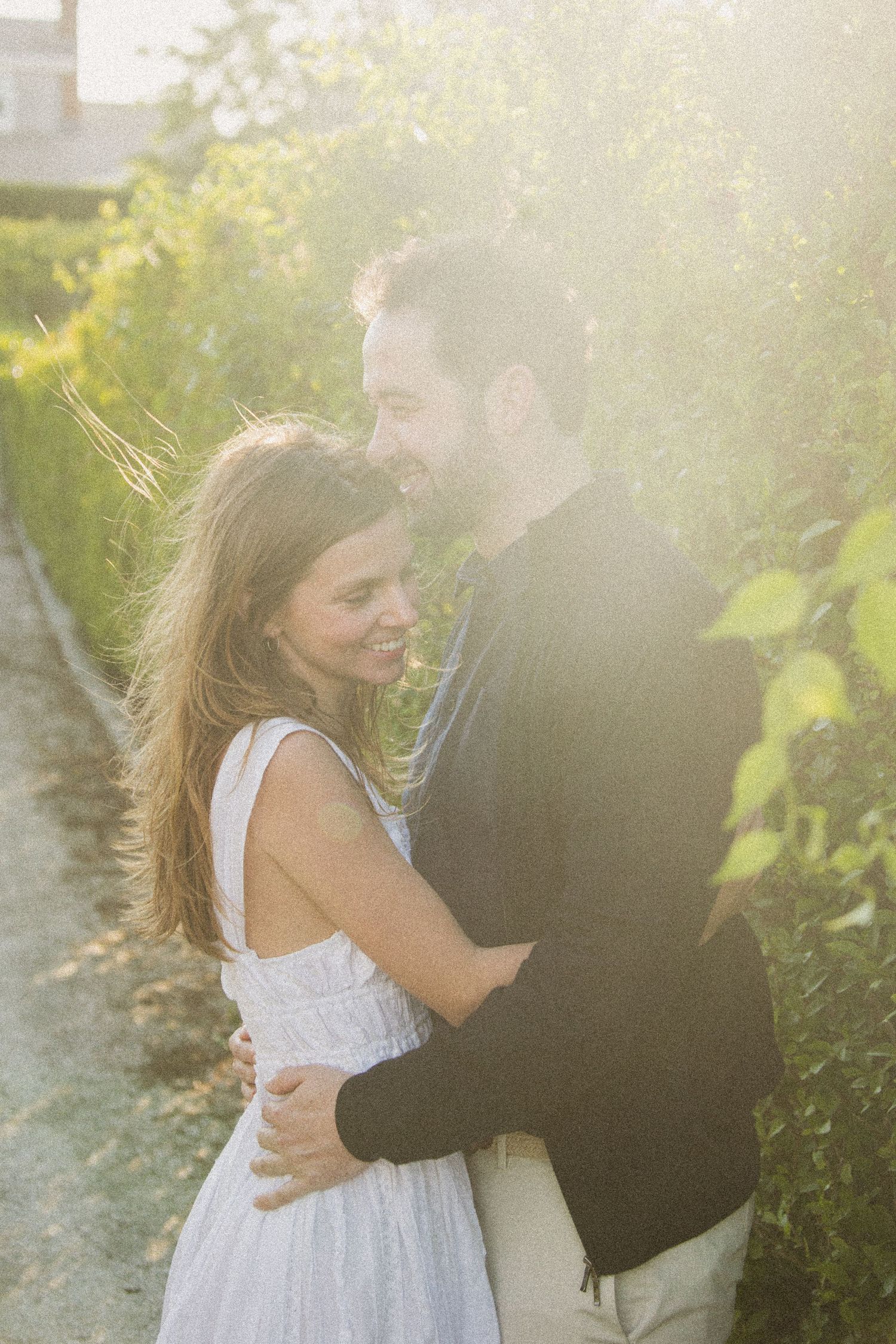 A romantic embrace captured in dreamy sunlit garden setting.