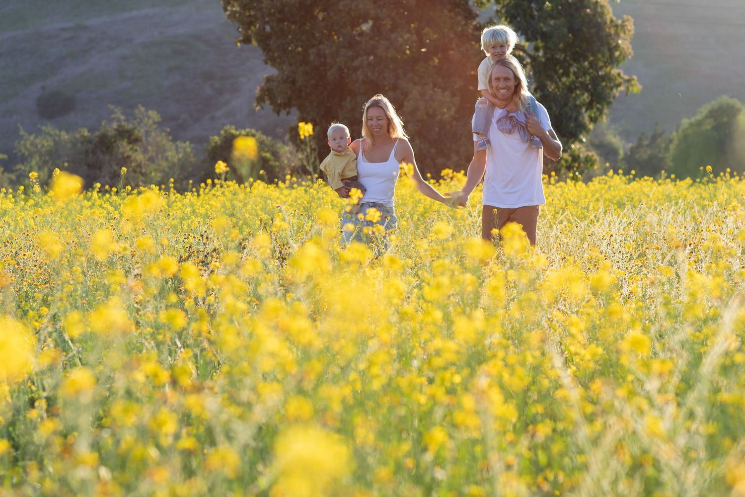 People walking through a field of bright yellow wildflowers at sunset.