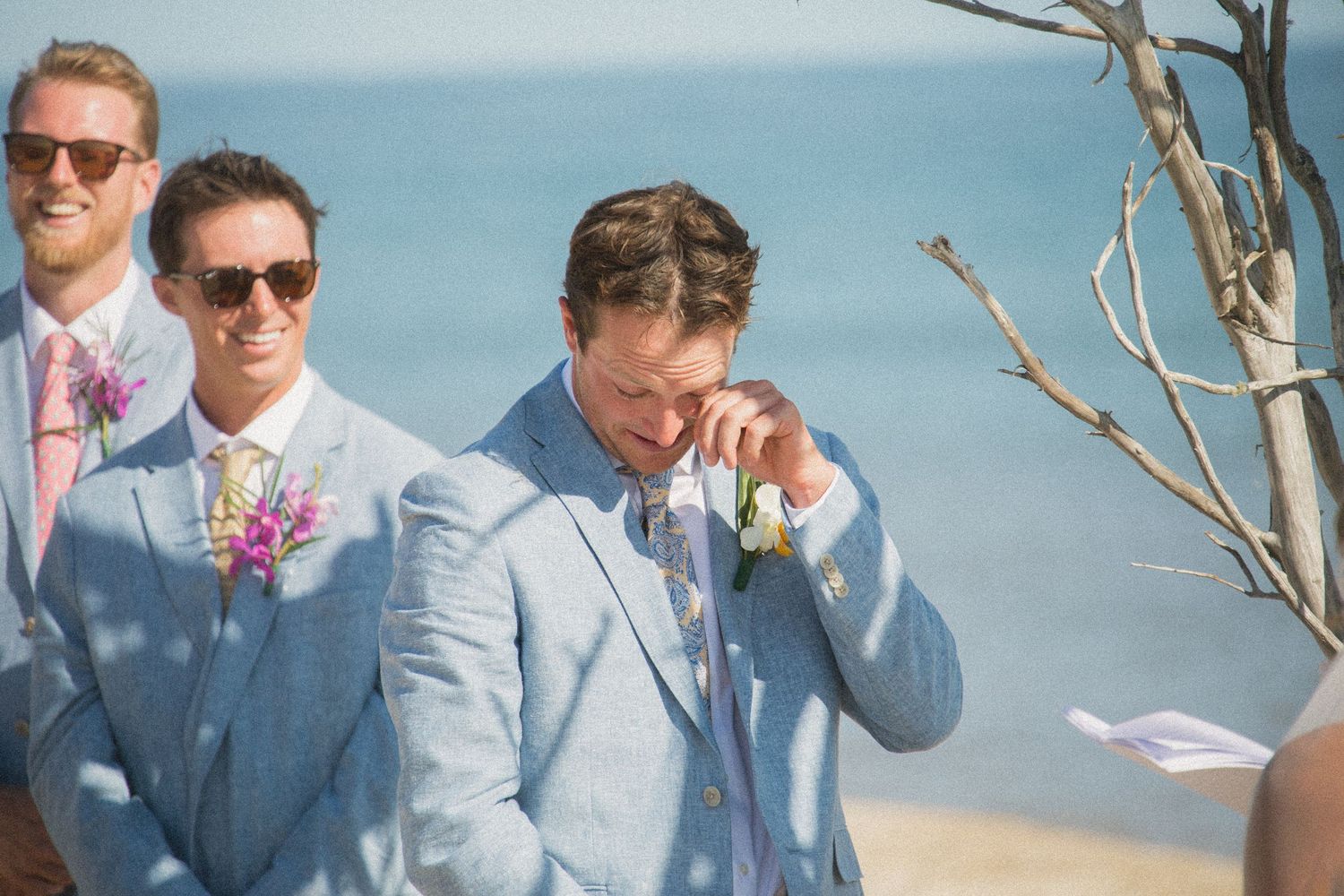 Groomsmen in light blue suits posing on beach with ocean in background.