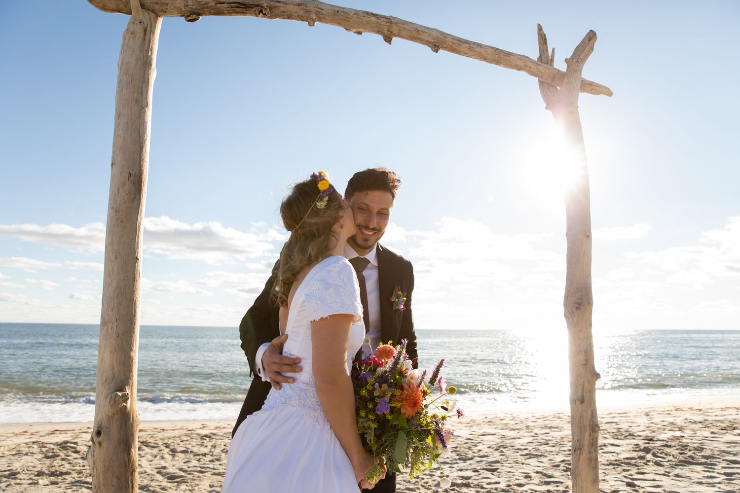 Sun-drenched beach wedding ceremony with natural driftwood arch and ocean views.