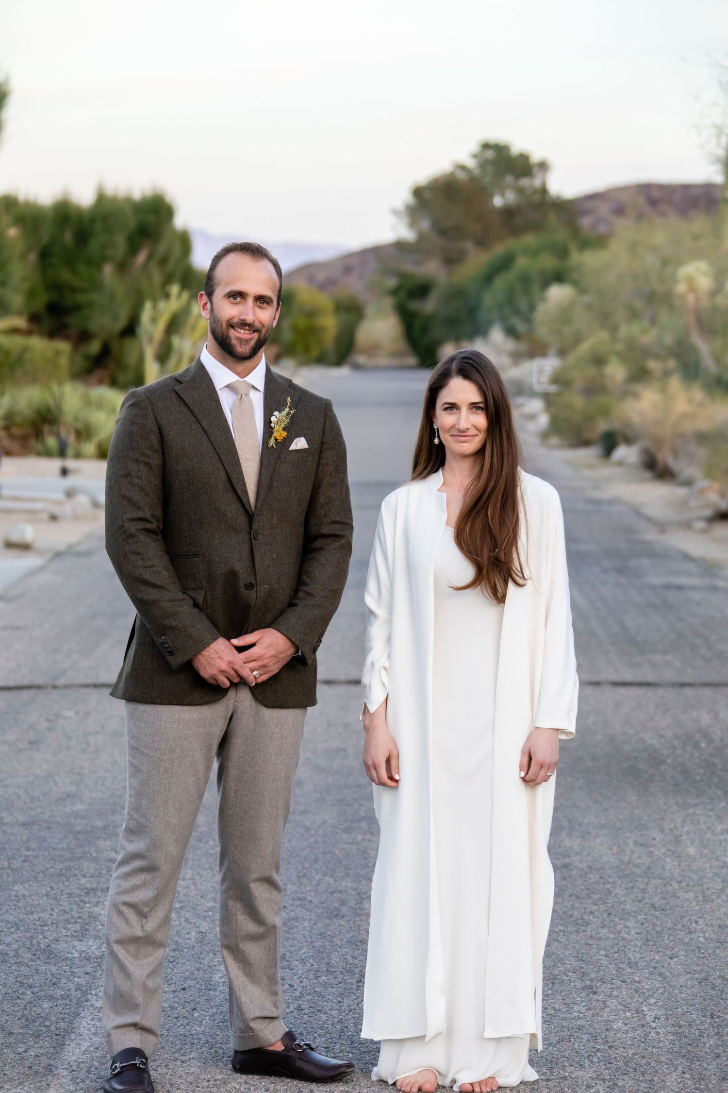 Wedding portraits on a desert road with mountains and vegetation in background.