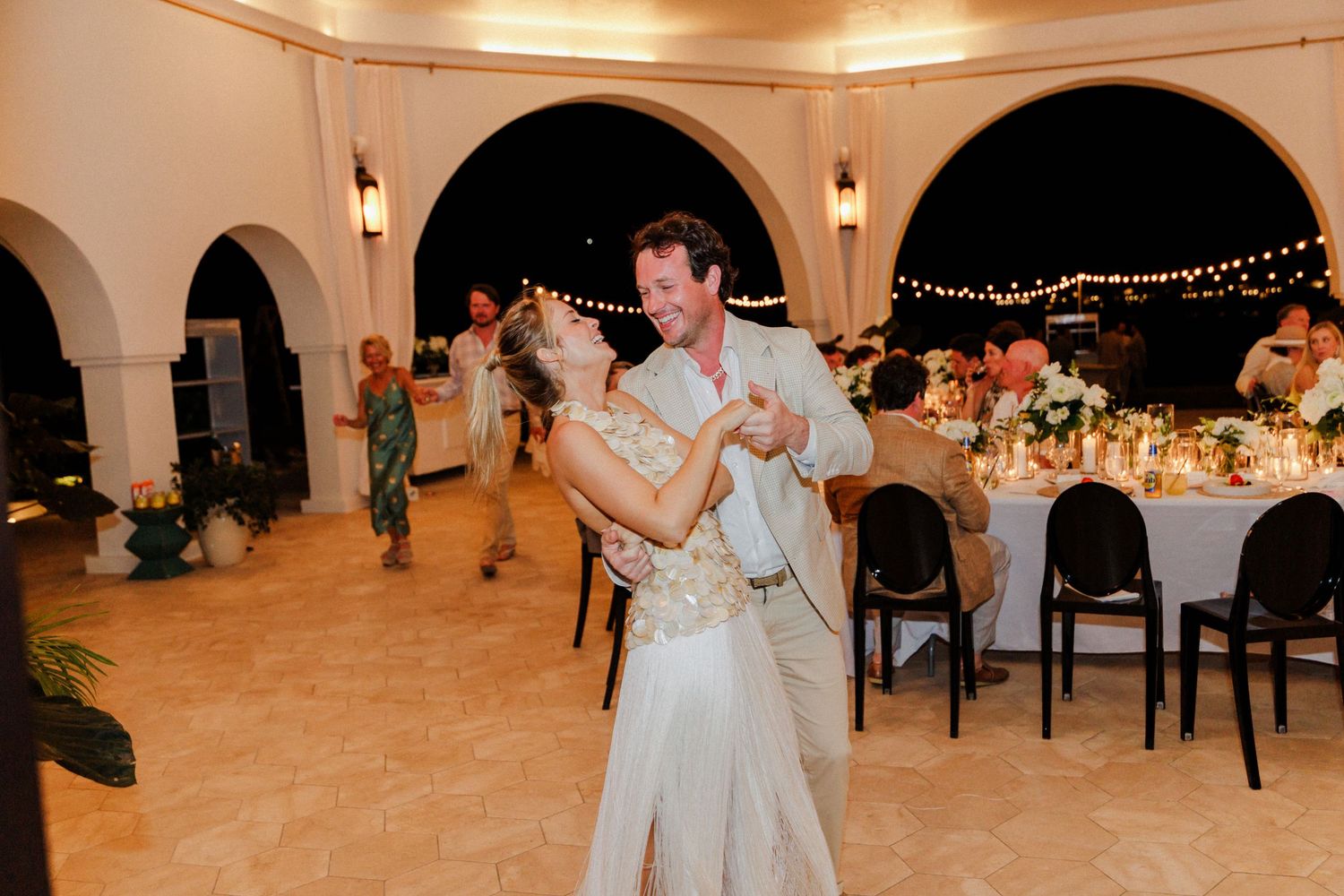 Wedding guests dancing and celebrating on an elegant dance floor under string lights at an indoor reception.