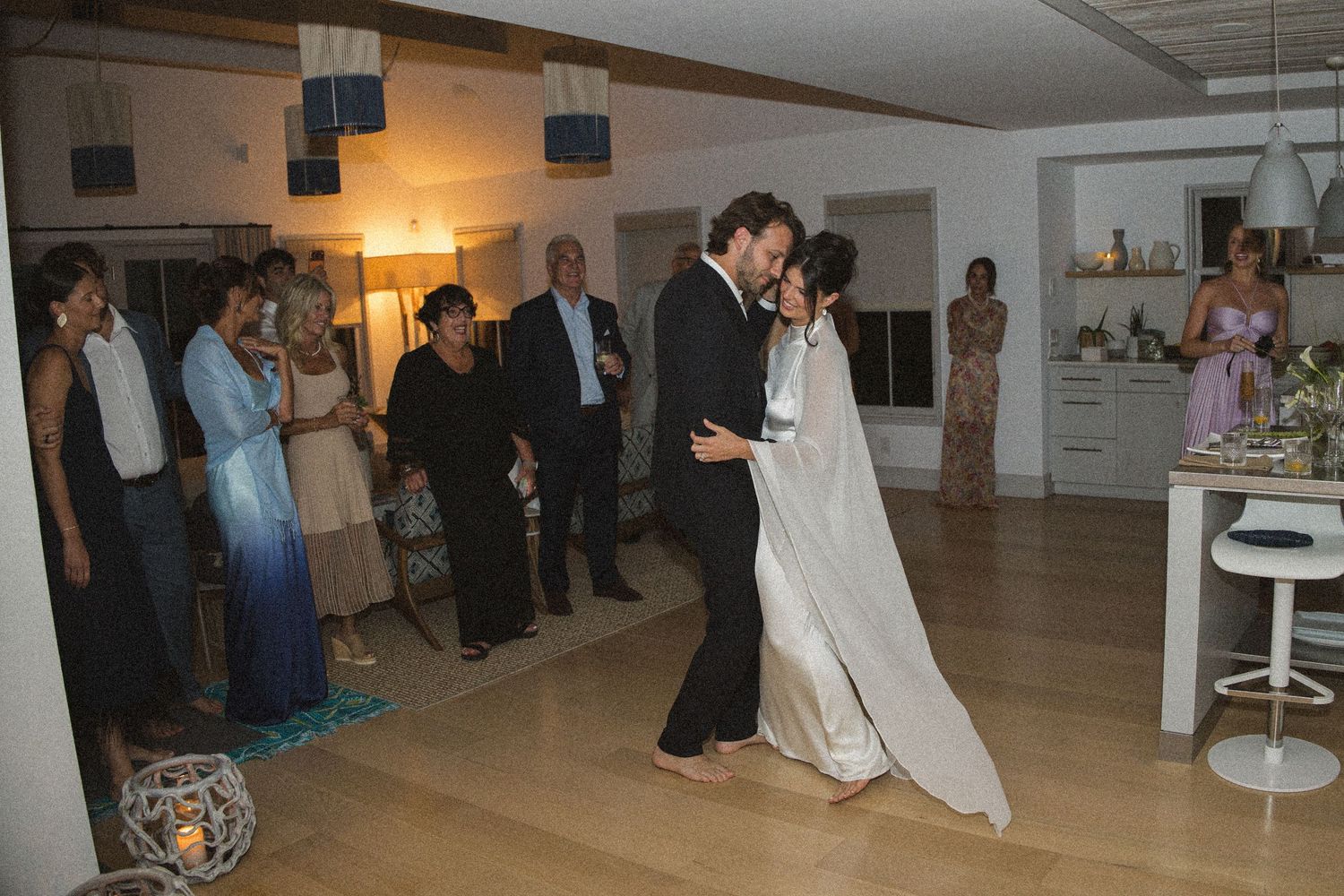 Bride and groom share their first dance at an intimate indoor wedding reception surrounded by guests.