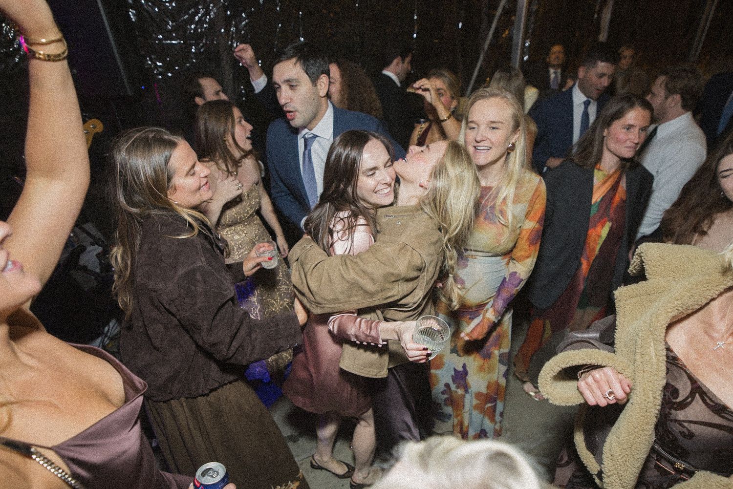 Smiling wedding guests hug and celebrate together on the dance floor as friends in formal wear look on.