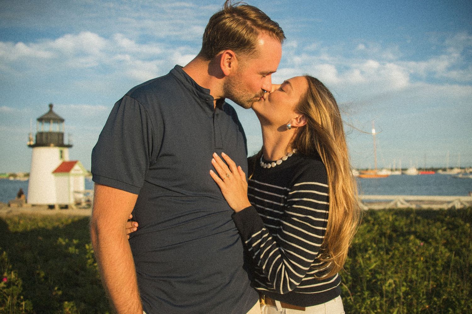 Romantic couple sharing intimate moments at sunset near a lighthouse with ocean views.