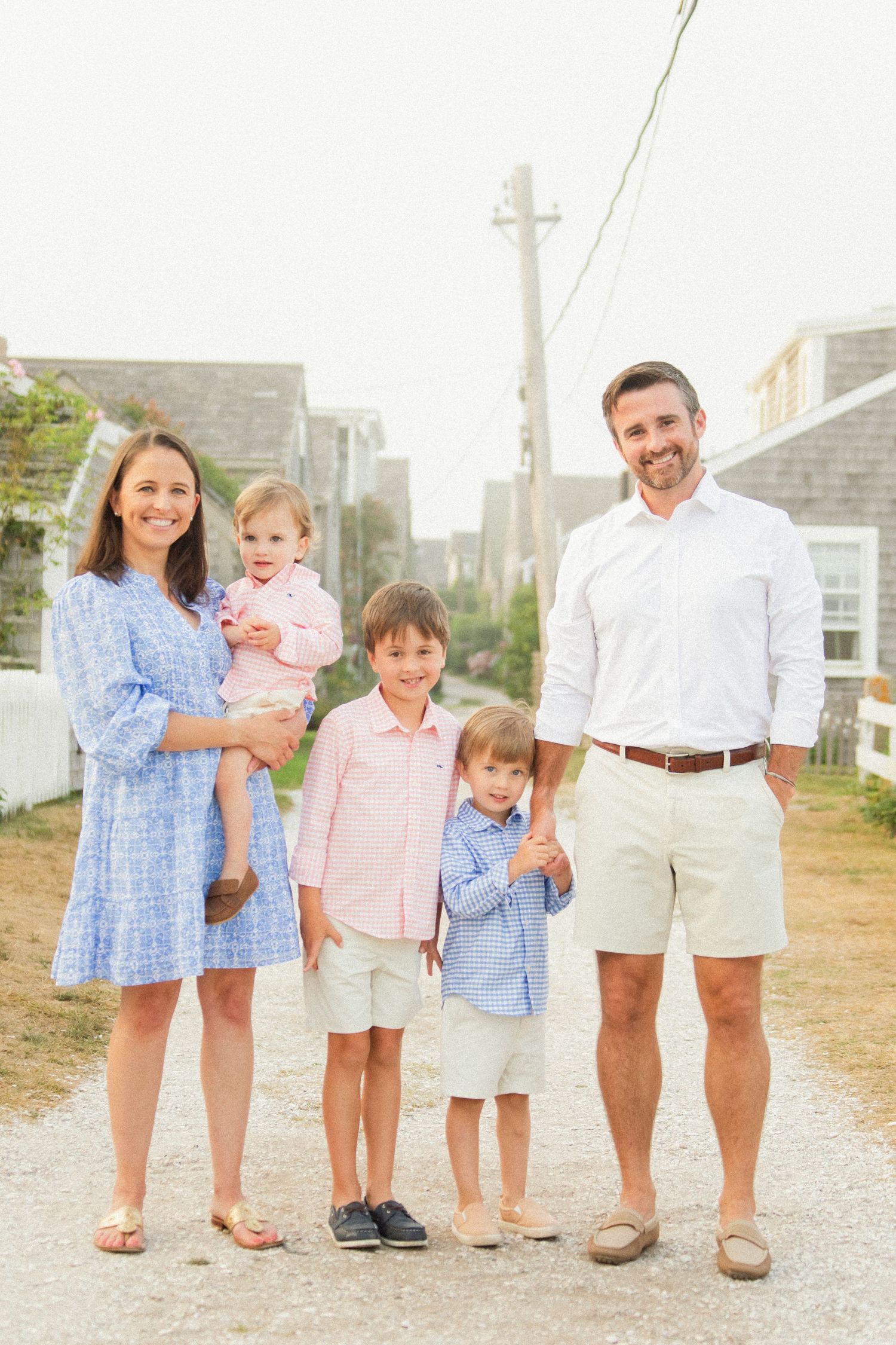 A family stands together on a gravel path with classic New England cottages in the background.