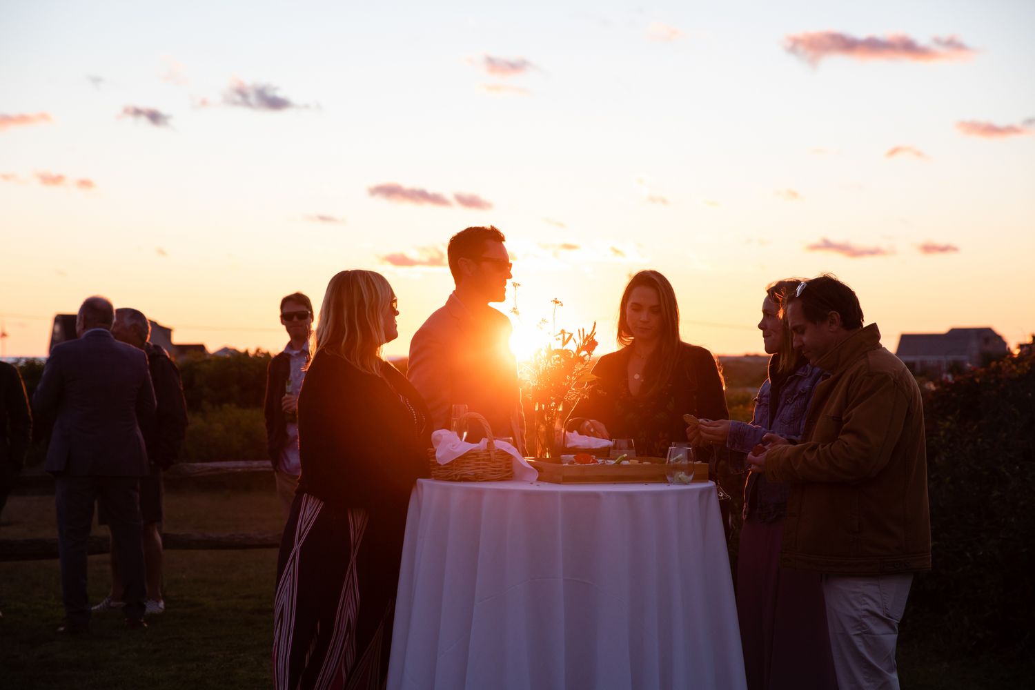 Guests gather around a cocktail table at sunset during an outdoor reception.