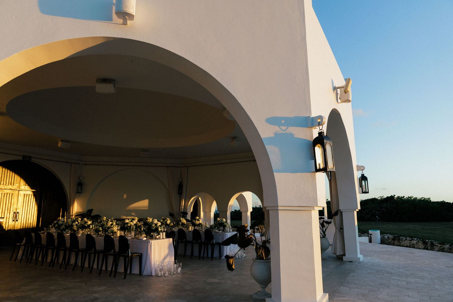 Wedding reception setup under white arched colonnade at sunset.